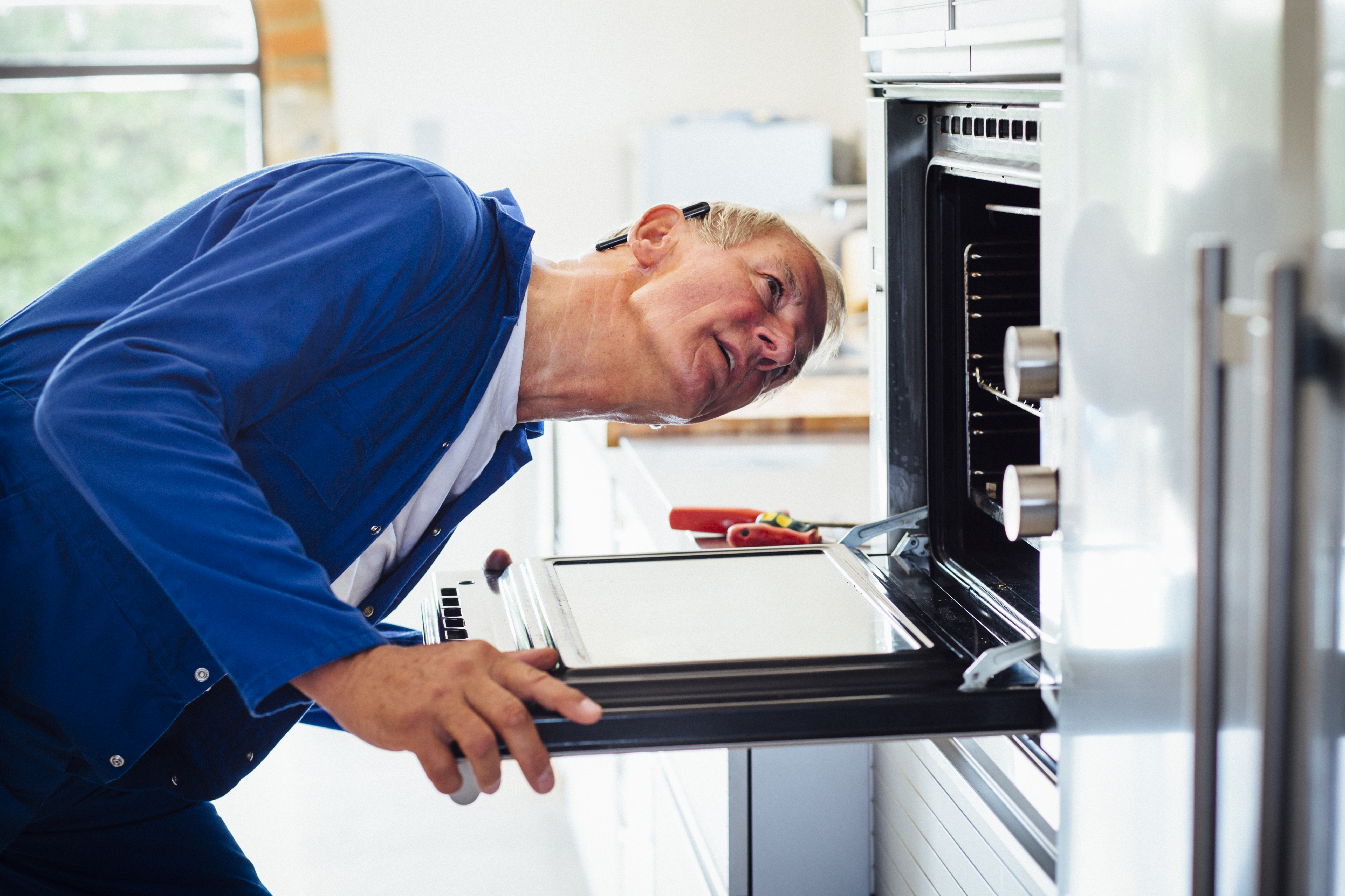 Man in a blue shirt looking inside of a wall oven 