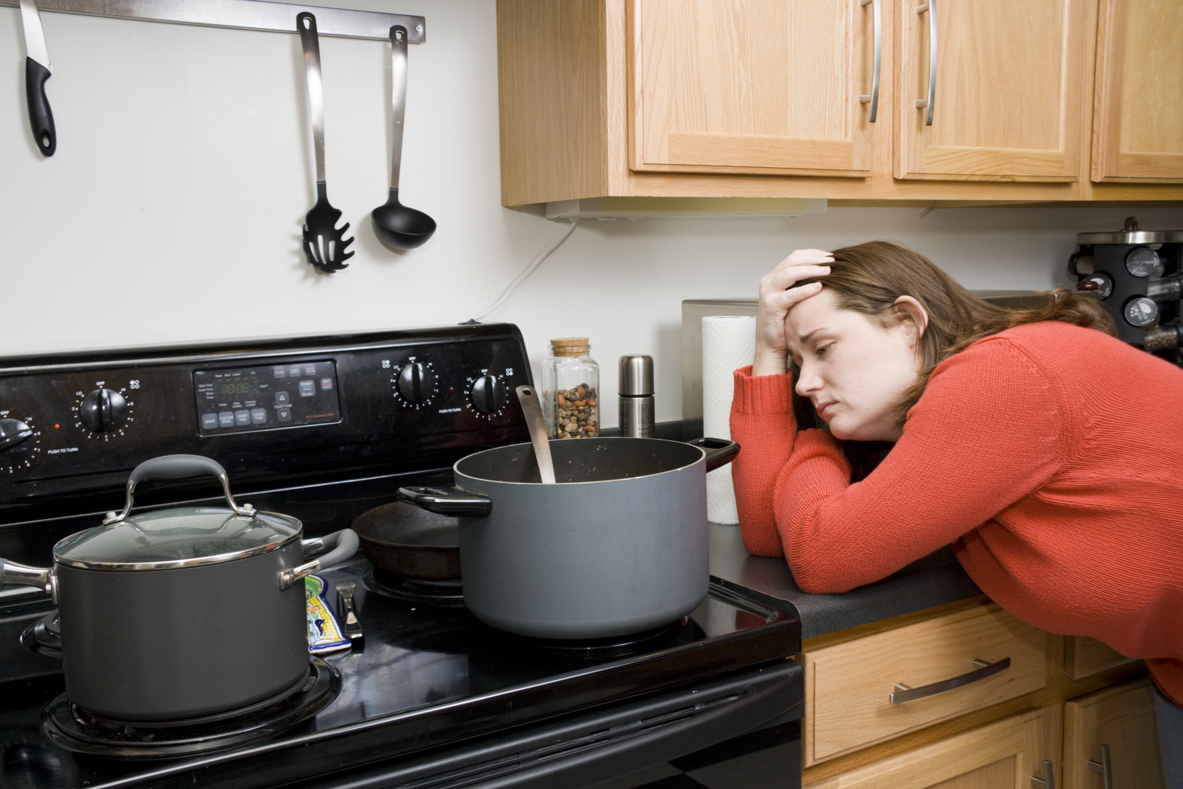 Woman in a red shirt grimaces at a pot cooking on an ceramic coil range 