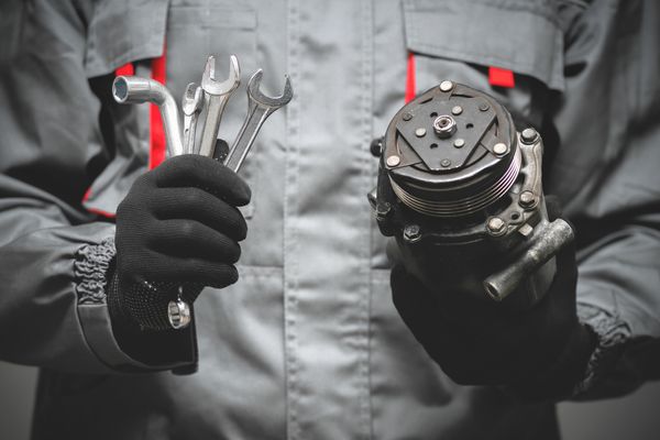 A repair technician holding tools and an appliance part 