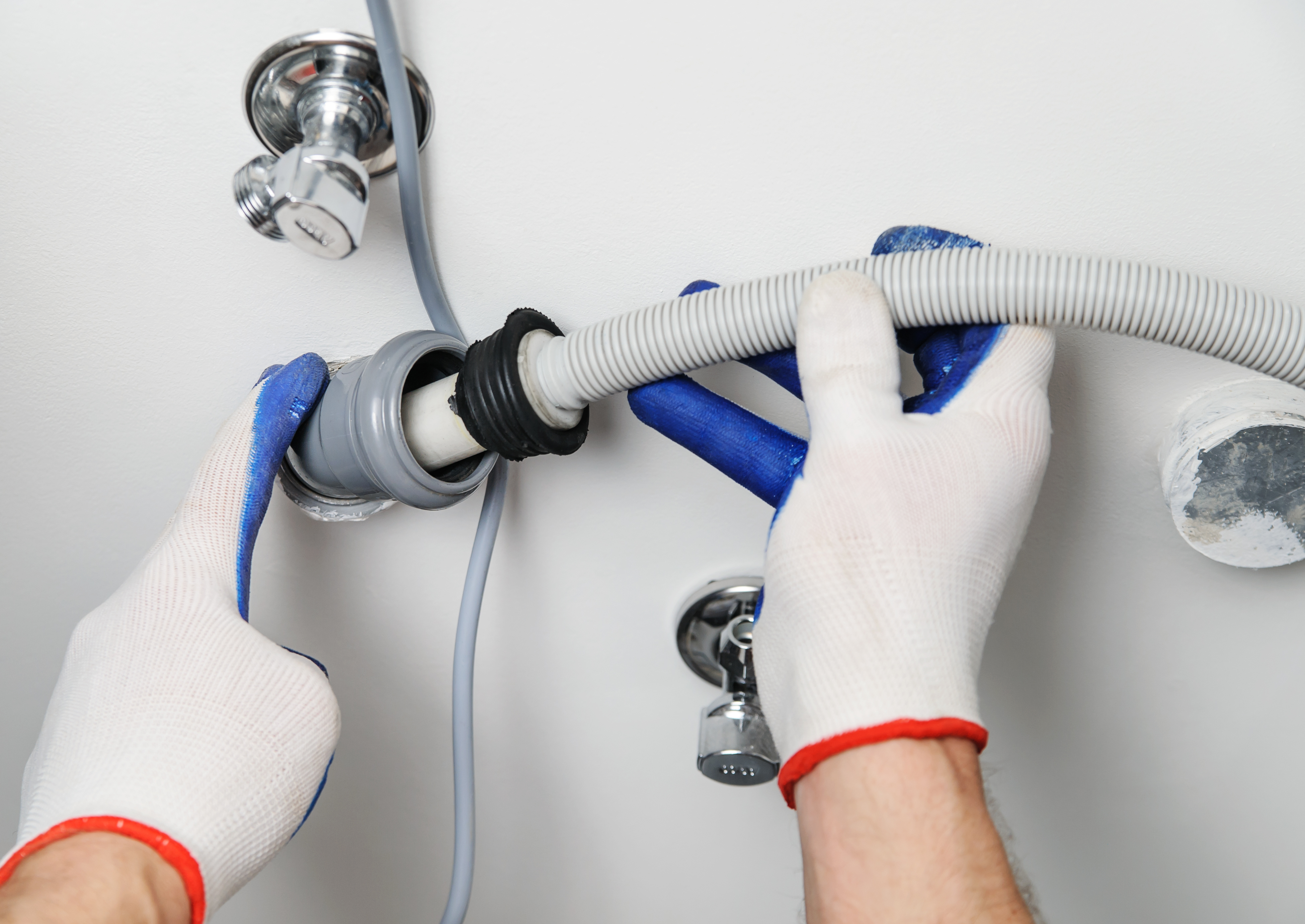 A person with gloves inserting a washer hose into the drain 
