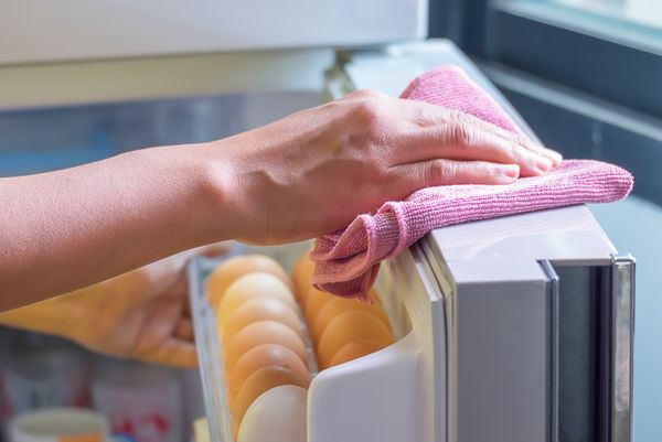 A person cleaning a refrigerator door with a pink microfiber cloth