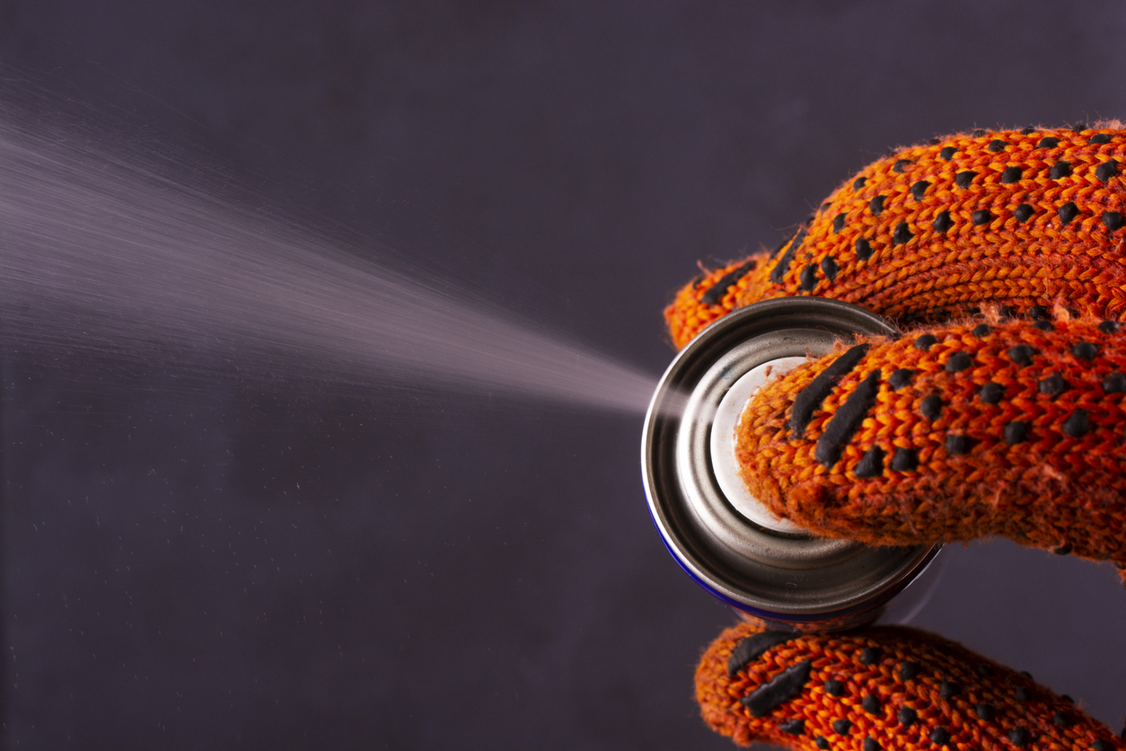 person with orange gloves sprays aerosol from can