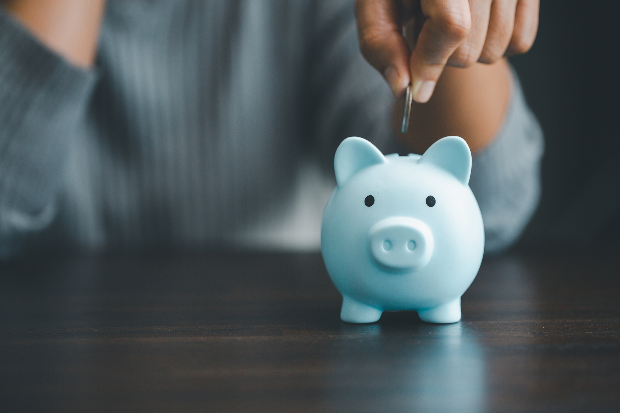 A person inserting a coin into a blue piggy bank 