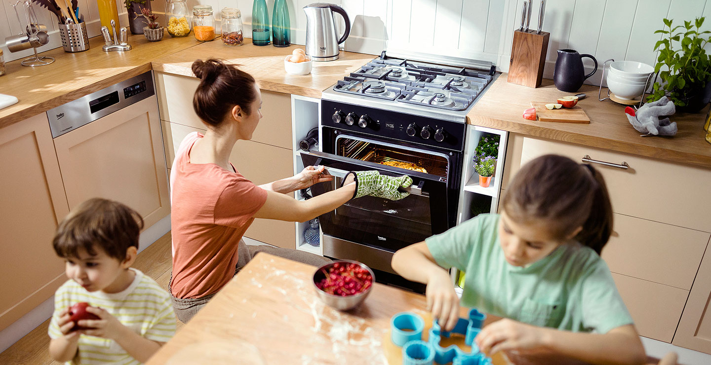 A woman pulls food from her Beko range as her children play in the kitchen