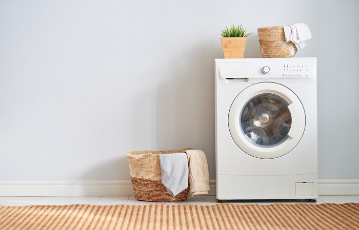 Washing machine with plant and basket on top in modern laundry room. 