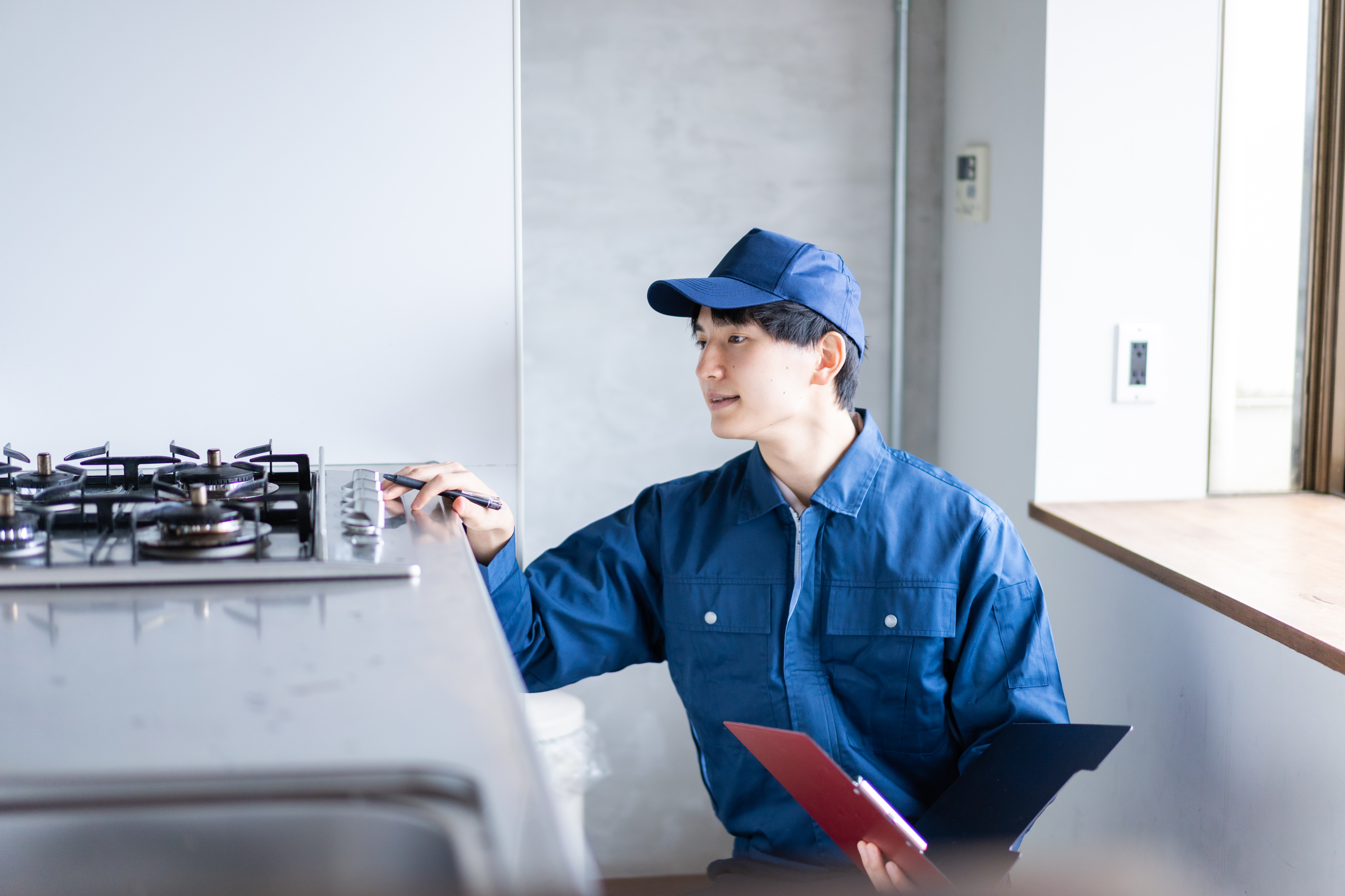 An appliance repairman in blue evaluating a gas cooktop 