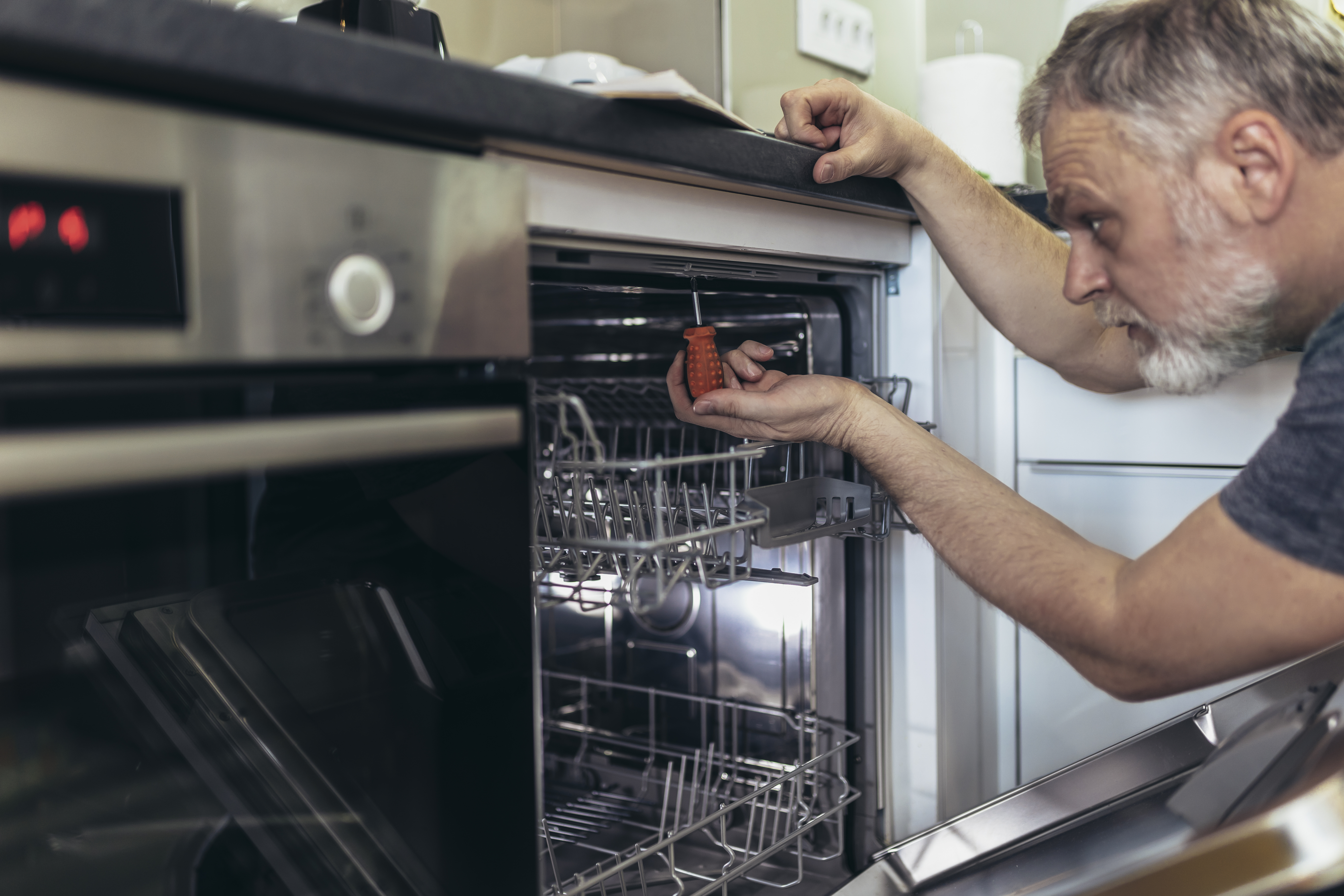 A middle-aged man installing a dishwasher 
