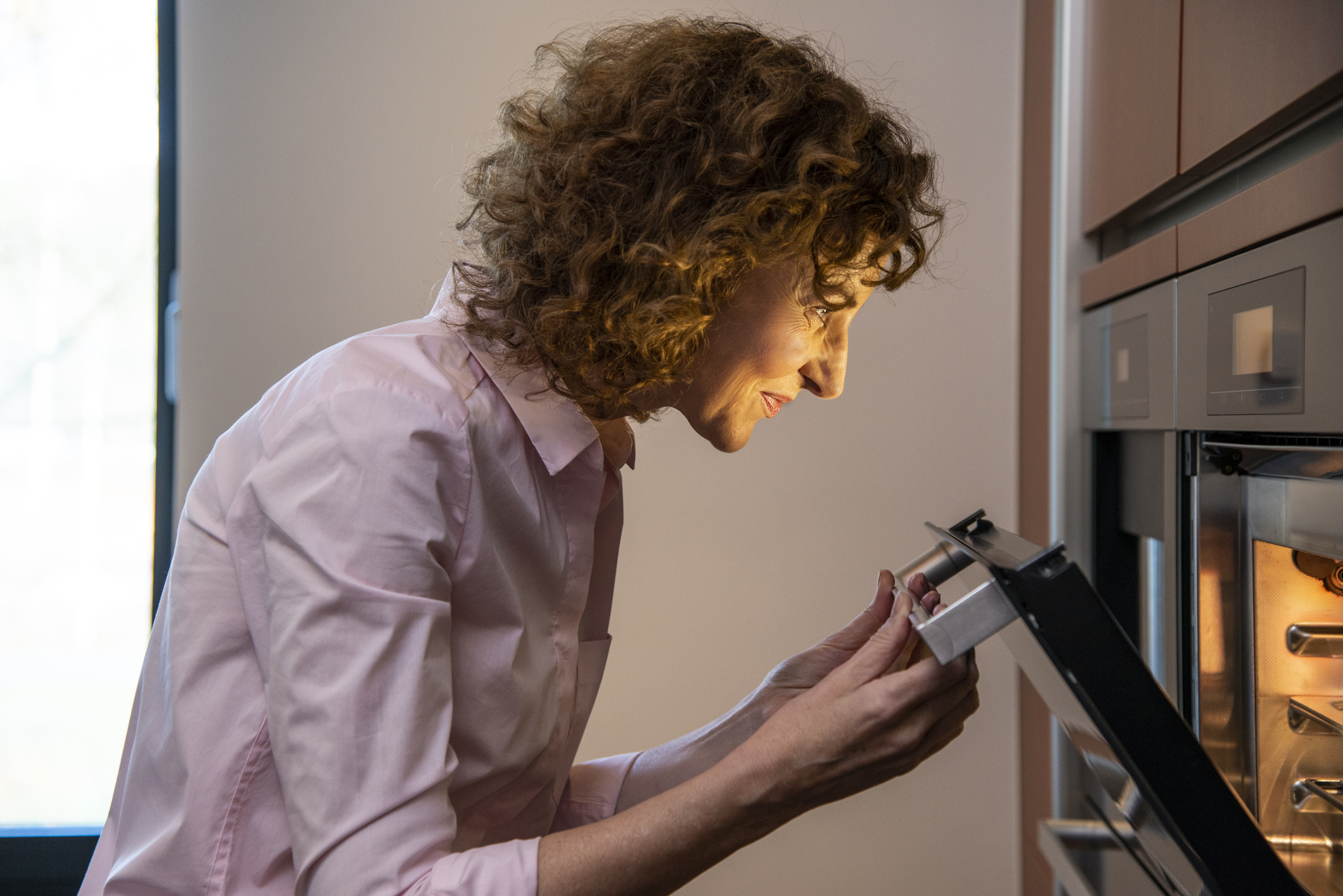 A woman smiling while peeking into an oven 