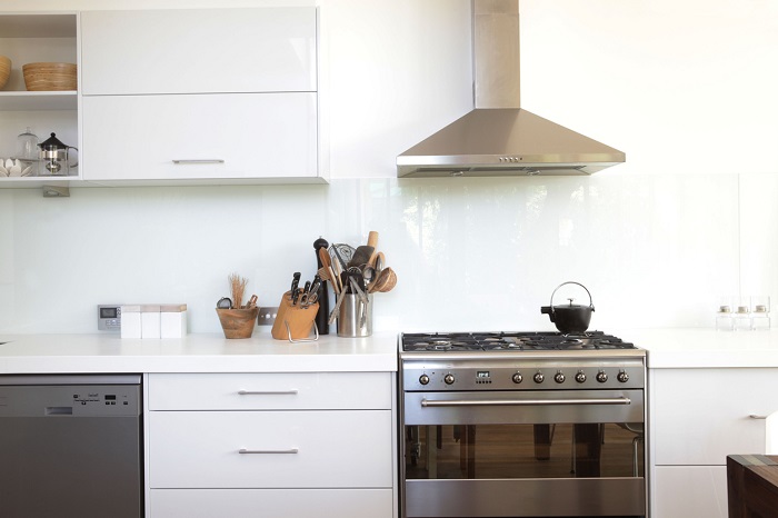 Contemporary white kitchen with stainless steel gas range and hood above. 