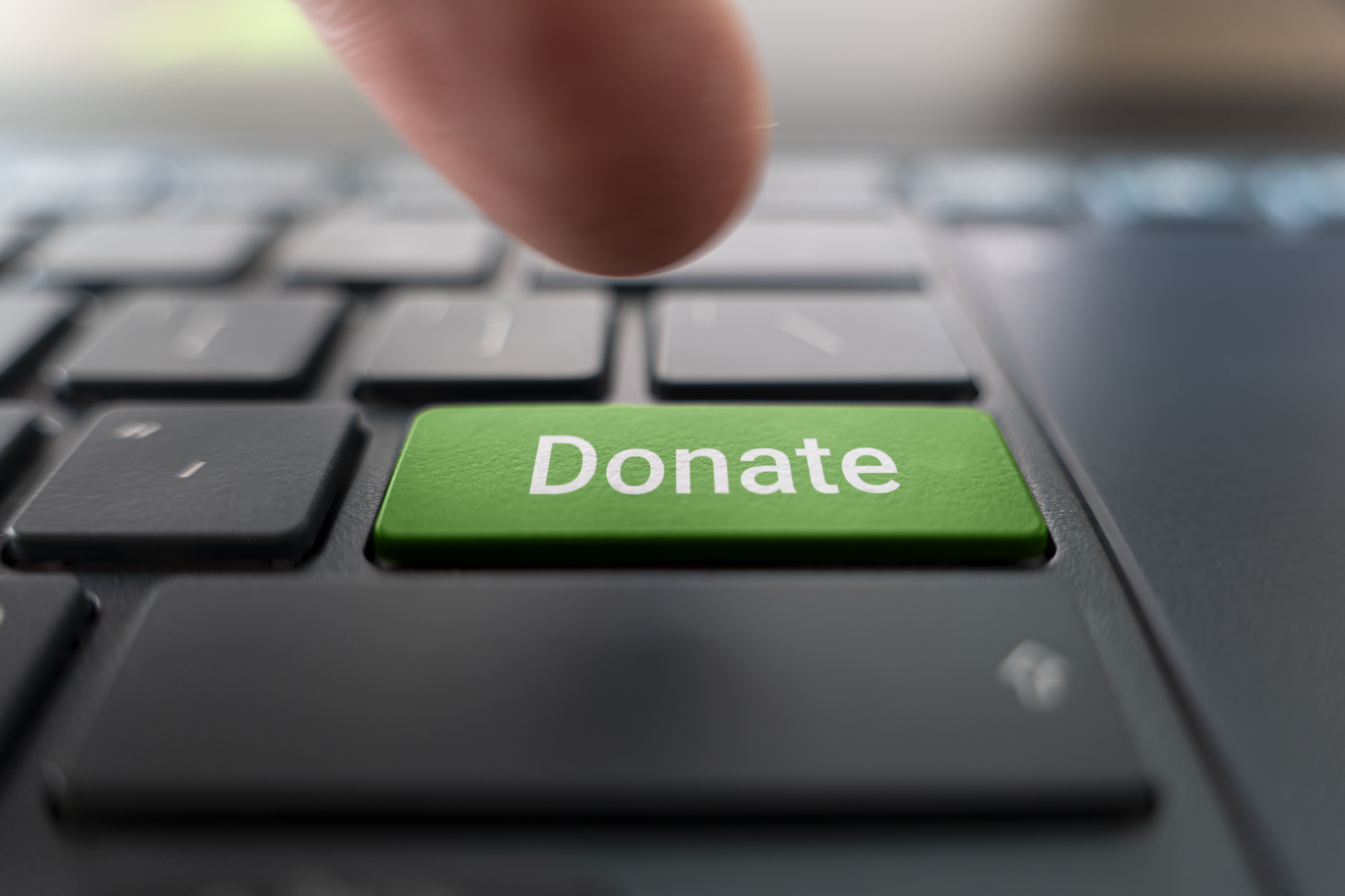 A person pressing a green donate button on a laptop 