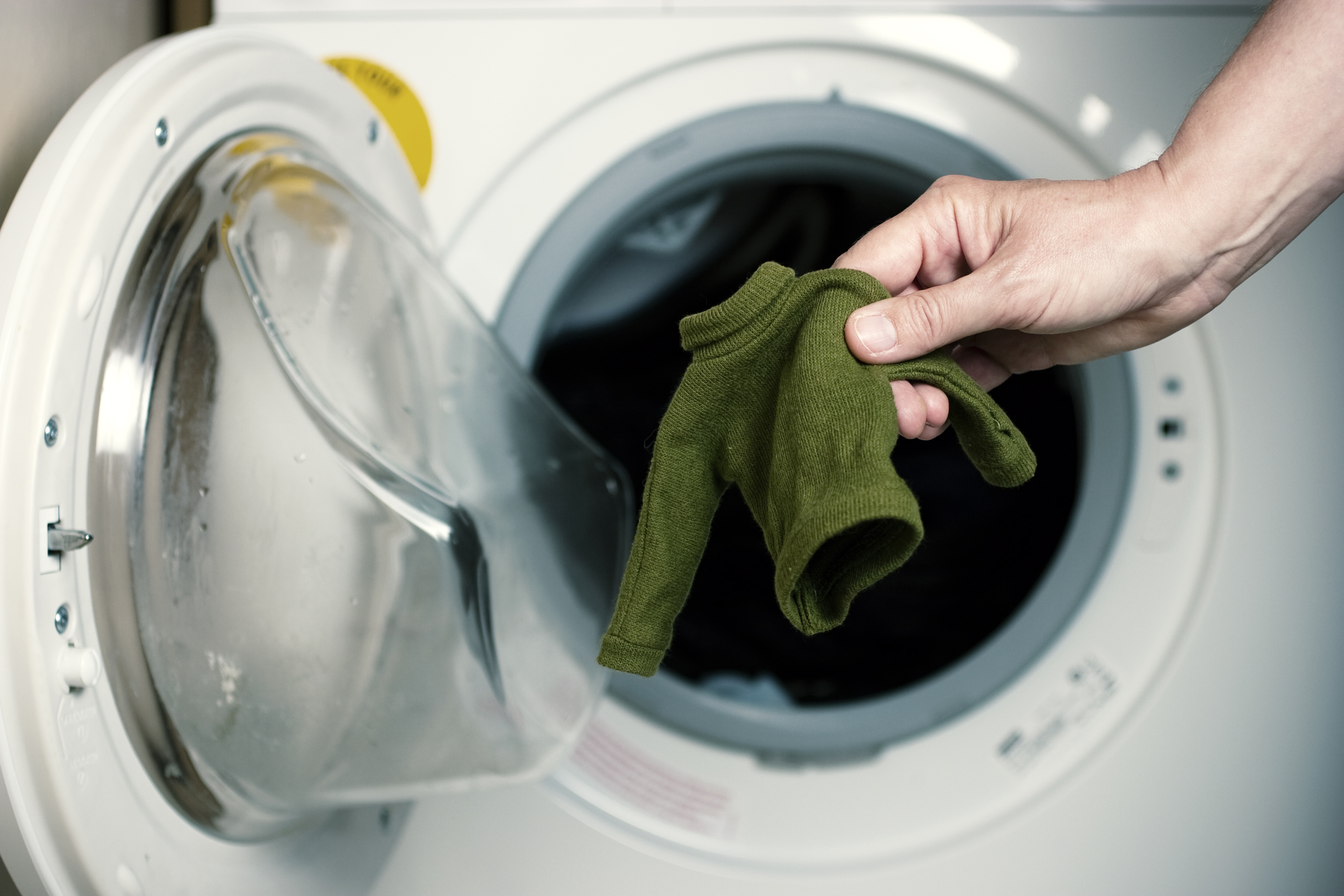 A person holding a shrunken green turtleneck sweater pulled from the dryer 