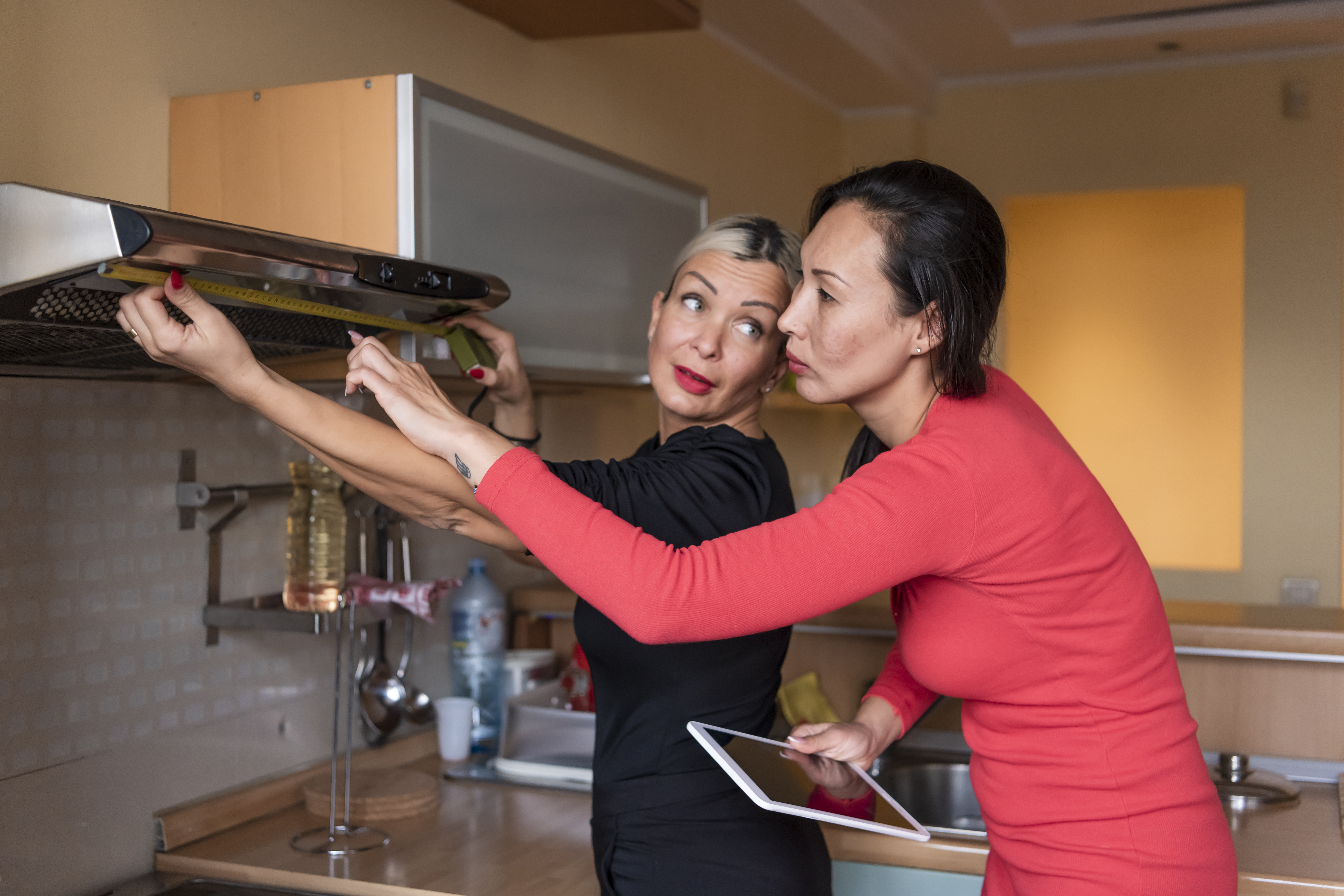 Two women measuring a range hood 