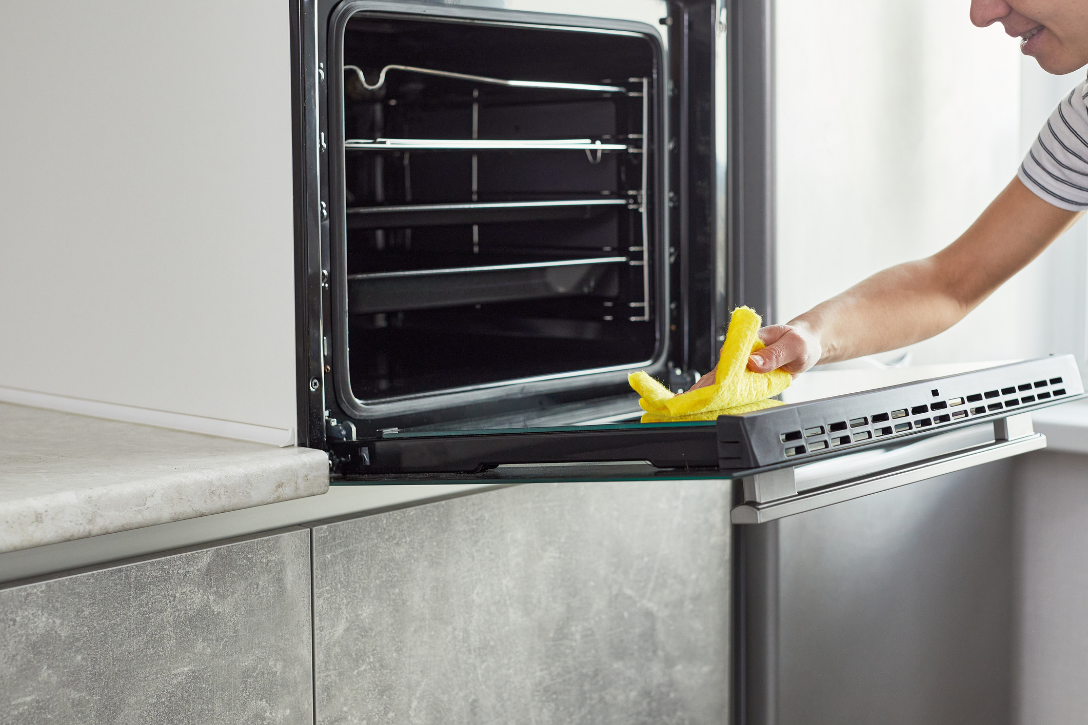 A woman wearing yellow gloves wiping down the interior of an oven door 