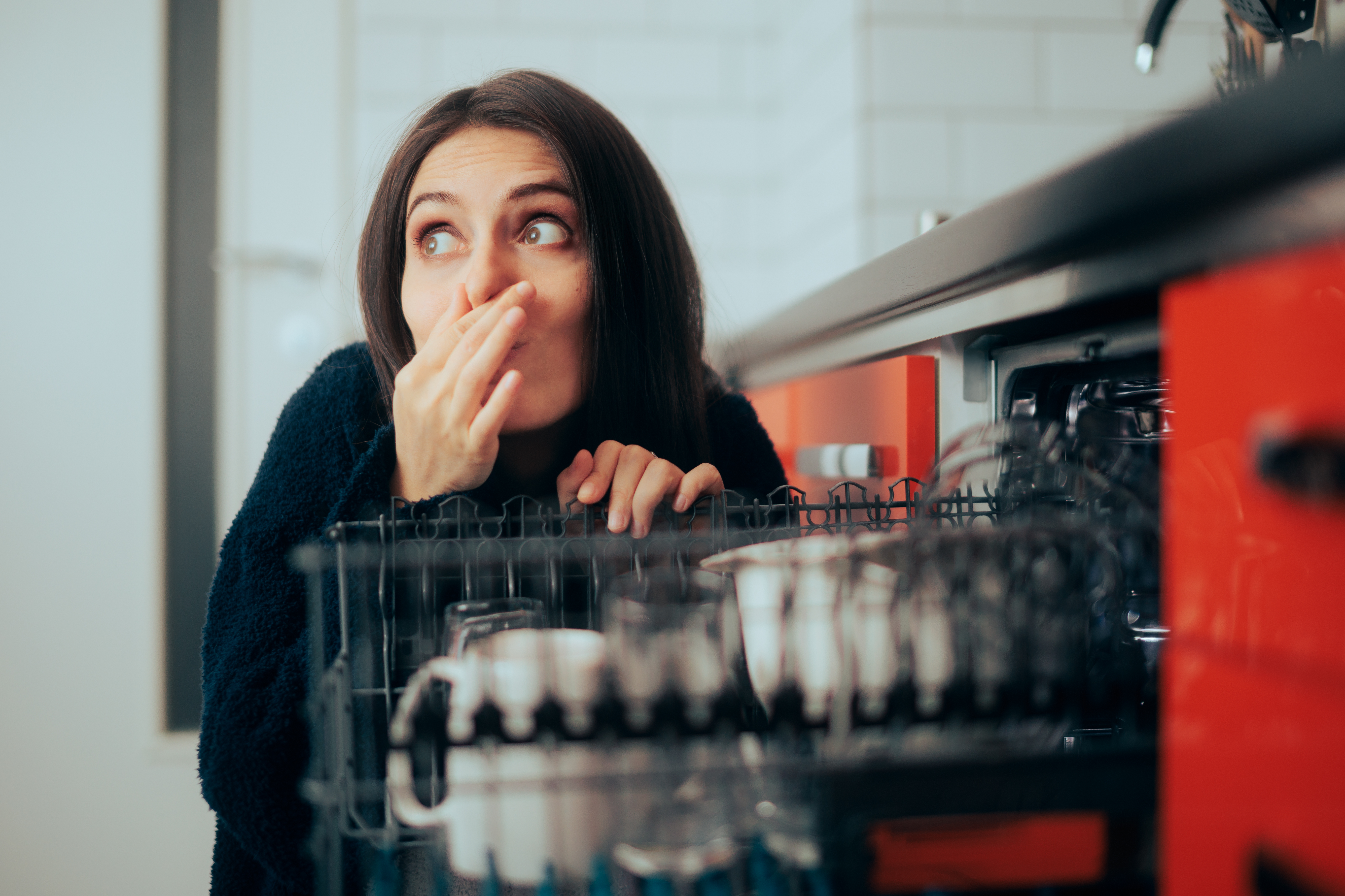 Woman plugging nose next to smelly dishwasher