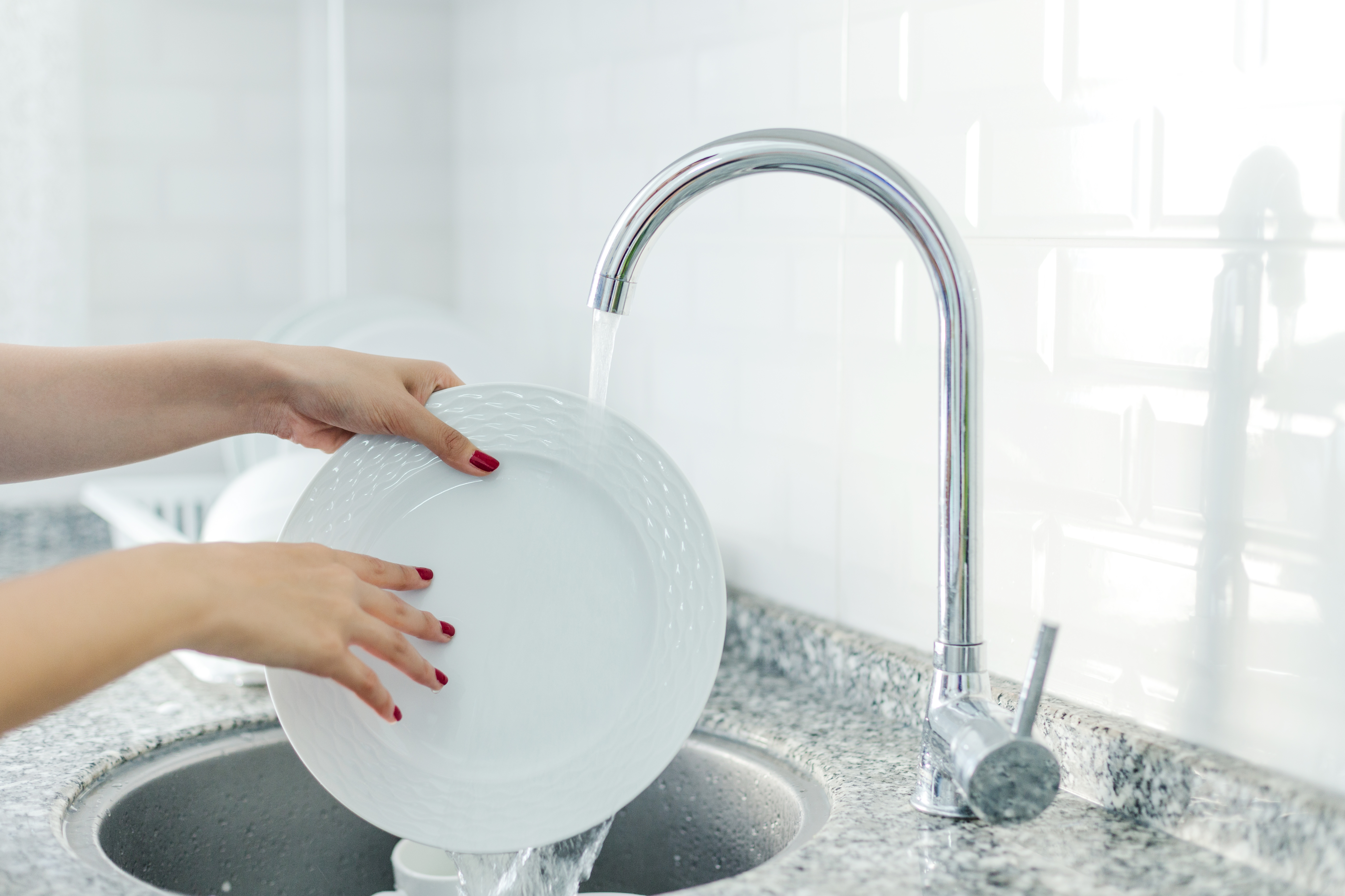 A person rinsing dishes under a faucet 