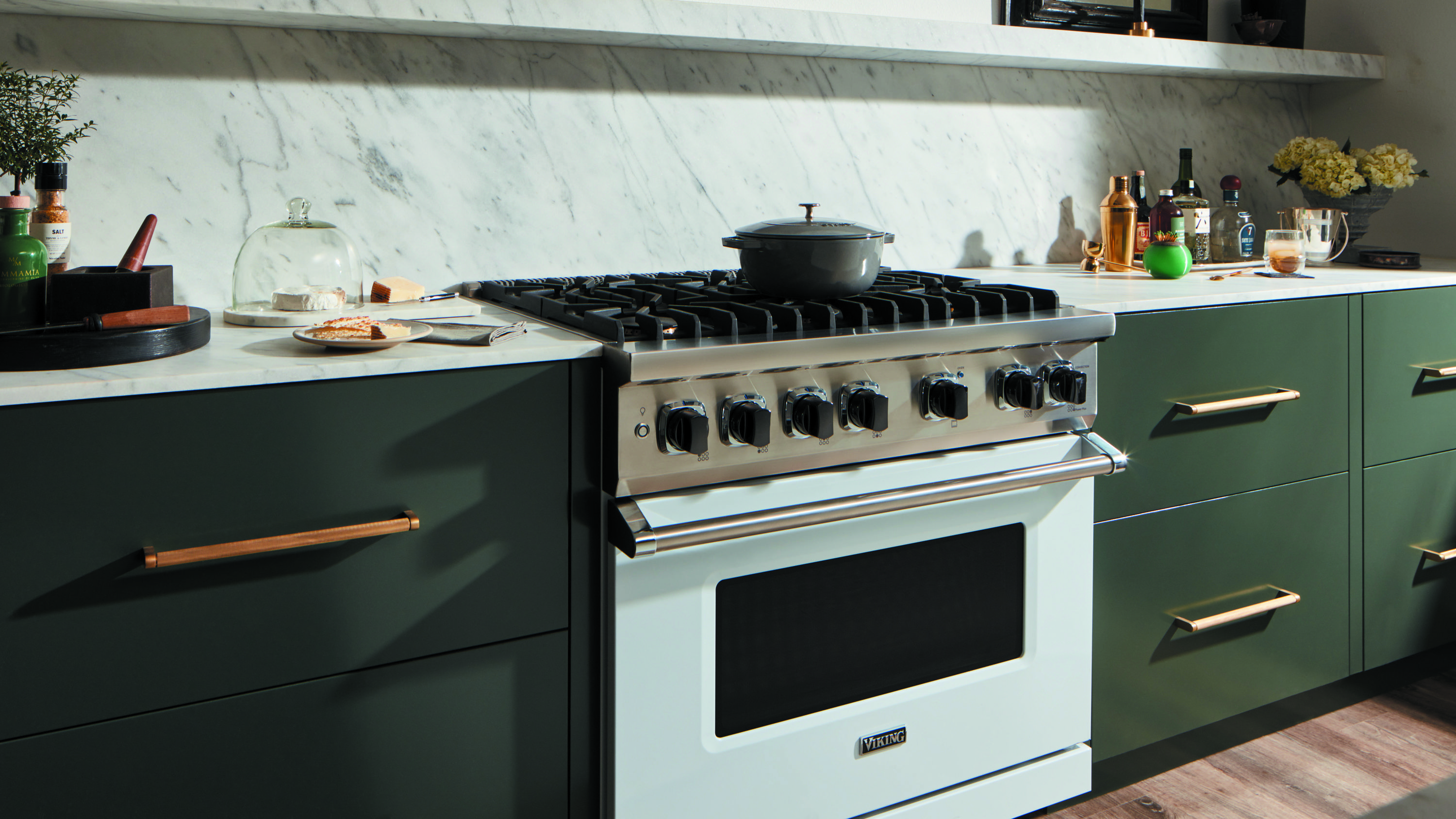 A white 36” Viking gas range featured in a kitchen with green cabinetry, gold hardware, and marble backsplash 