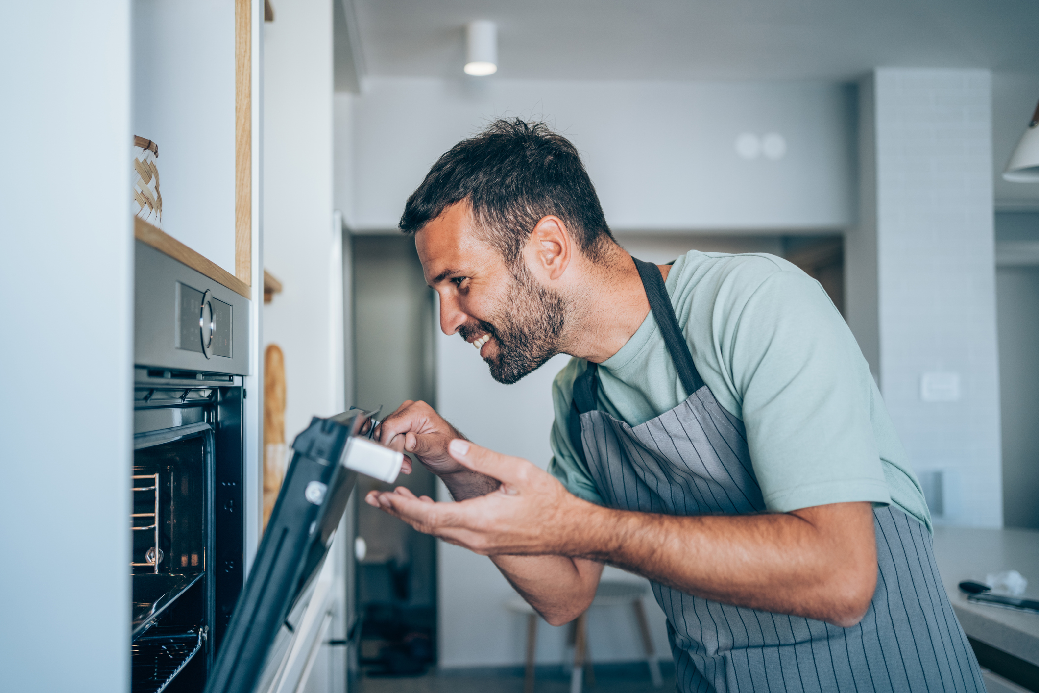Man in apron smiles as he looks inside a wall oven 