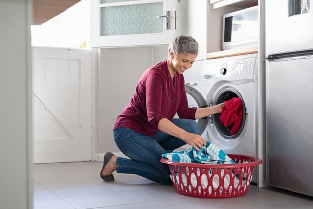 iStock Credit: Ridofranz Woman in burgundy shirt and jeans taking clothes out of front load washer