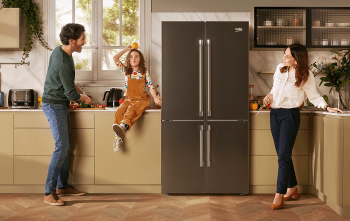 Couple playing with their small child on the kitchen counter next to a stainless steel Beko refrigerator. 