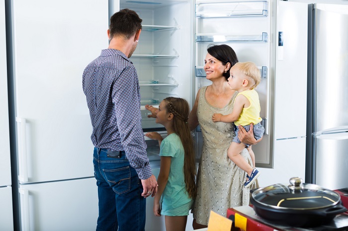 Happy young parents with two kids choosing a new freezer in a shop of household appliances.