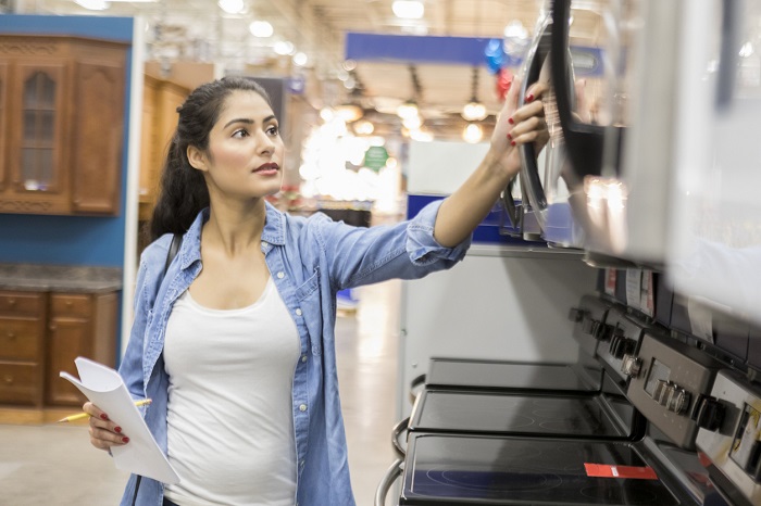 Young woman opens a microwave oven while shopping in a home improvement warehouse.