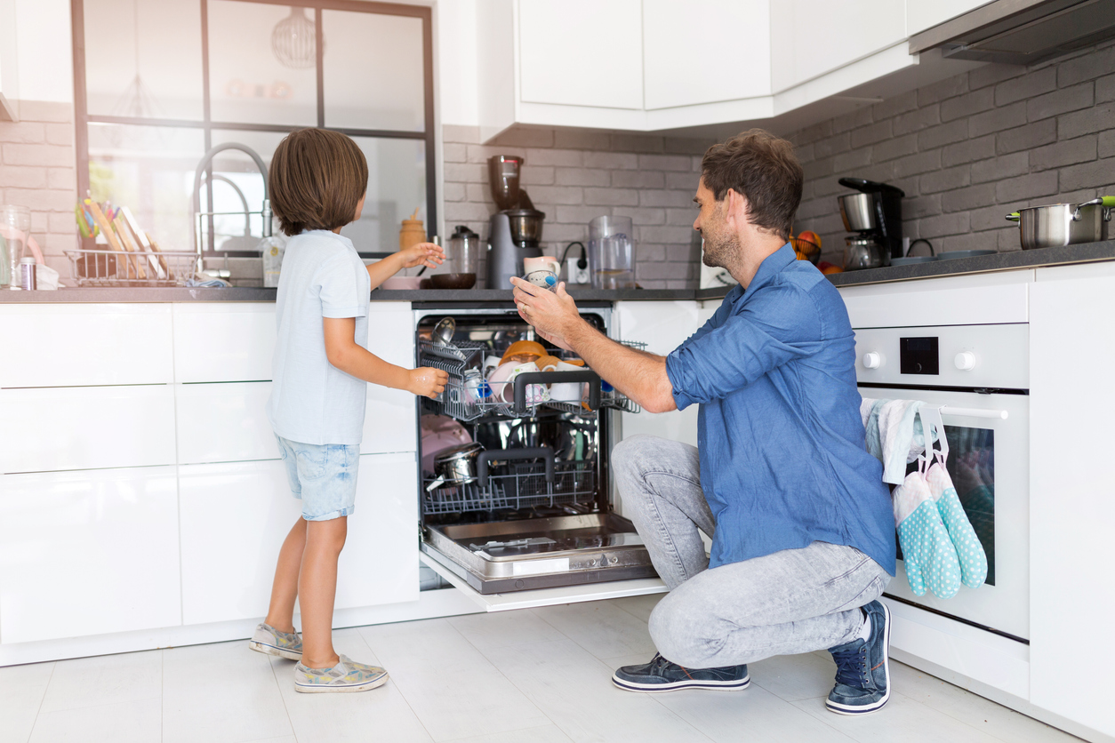 father and child unload clean dishes out of dishwasher 