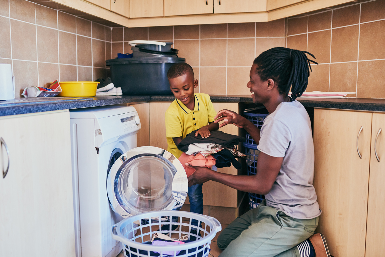 Father and son smile while they unload clothes from a front-loading washer 
