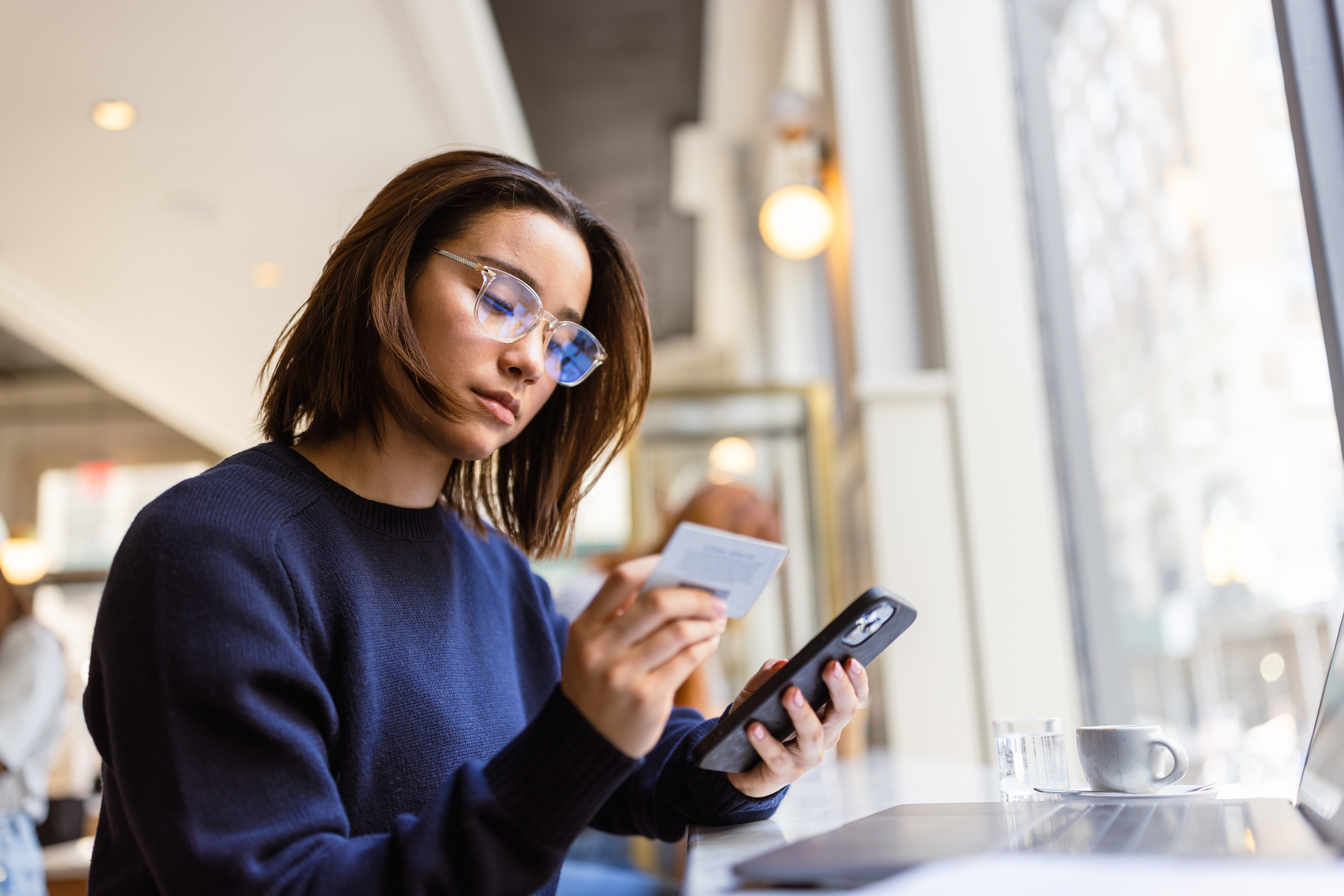 A young woman holding up a credit card while looking at a smartphone 