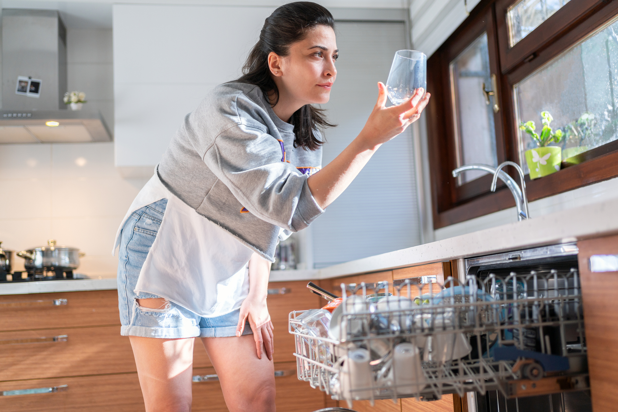 A woman inspecting a glass pulled from a dishwasher 