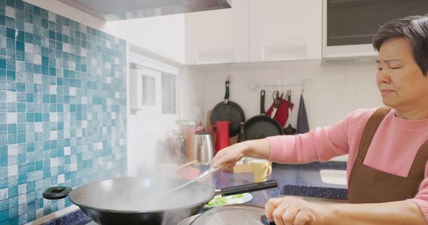 A woman cooking in a wok beneath a range hood 