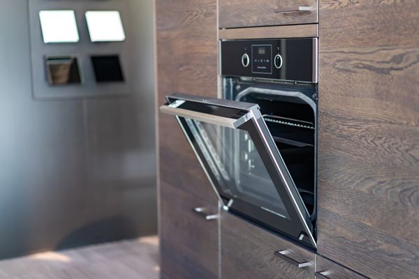 A black wall oven with an open door shown installed within a wooden wall 