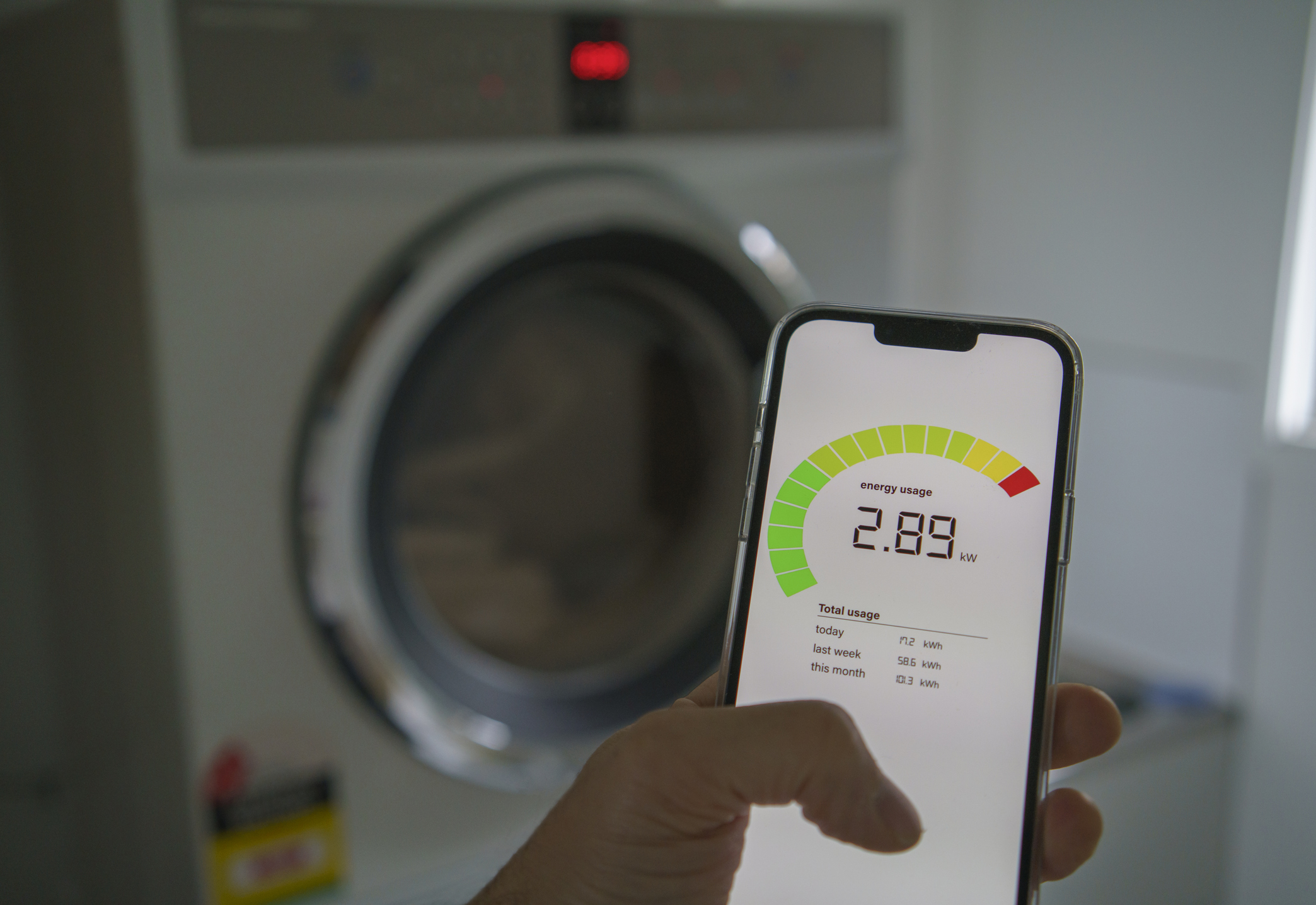 A front load washer in the background with a smart phone in the foreground with an energy rating on its screen
