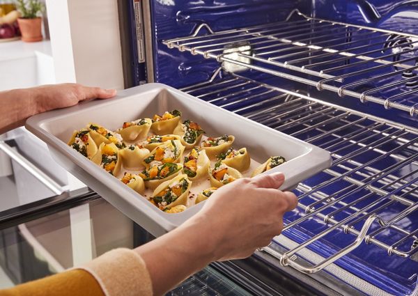 A person placing a casserole into a KitchenAid oven 