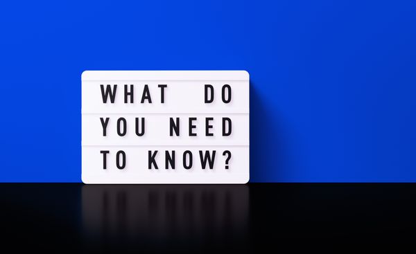 A black and white sign reading “What Do You Need to Know” against a blue and black background