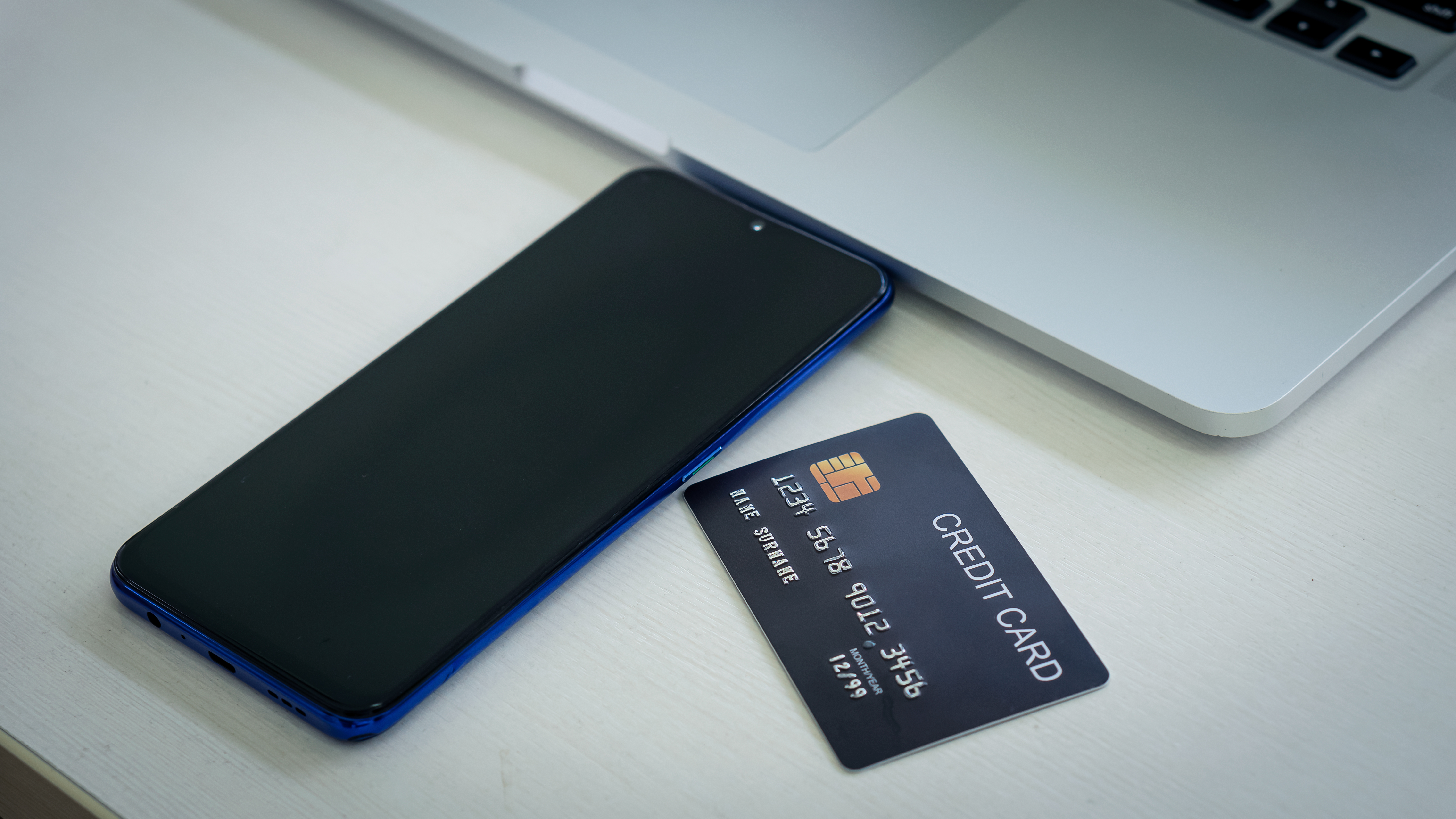 A generic credit card next to a smartphone and a laptop 