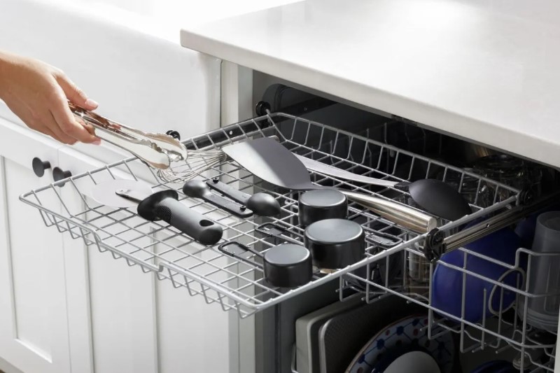 A hand places tongs onto the third rack of a GE dishwasher