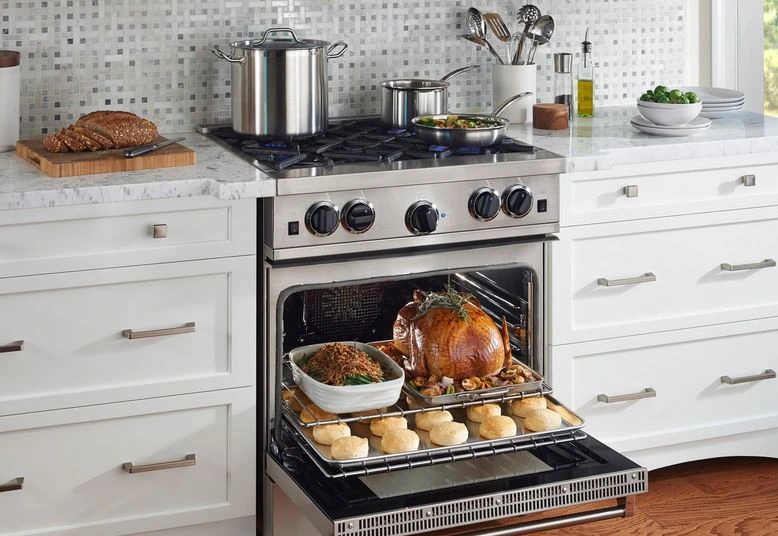 the BlueStar RCS30SBV2CF 30” gas range shown with its door open and with a full course meal 