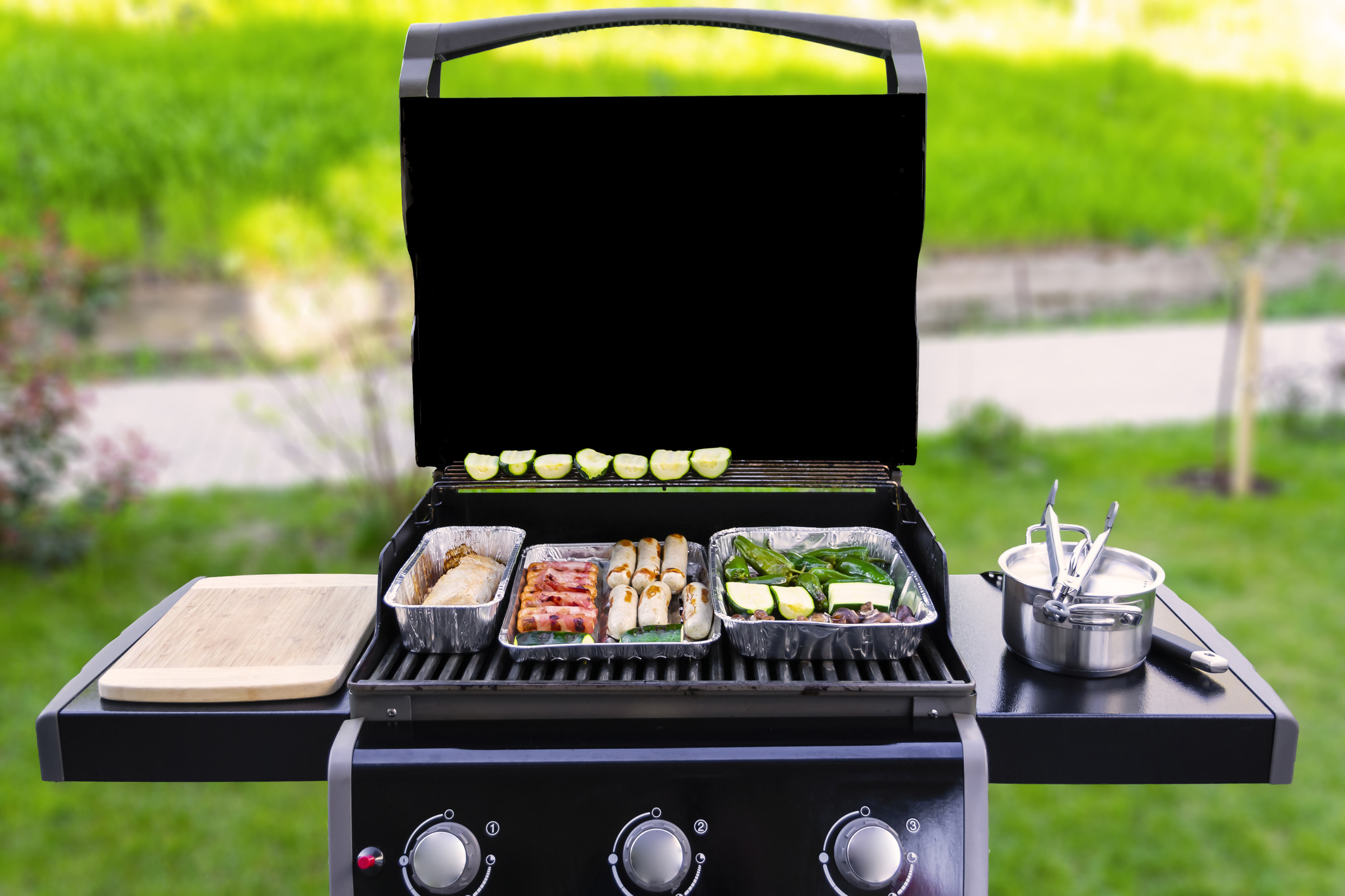 Wide shot of various foods cooking on a gas grill 