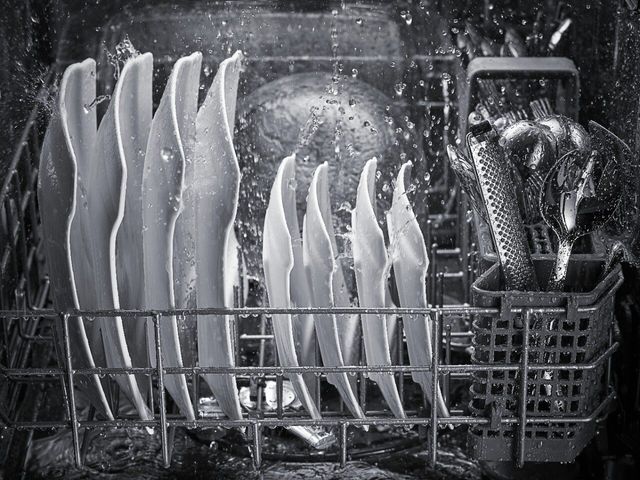 Close view of inside a dishwasher with plates and glasses in the racks and water being splashes around.