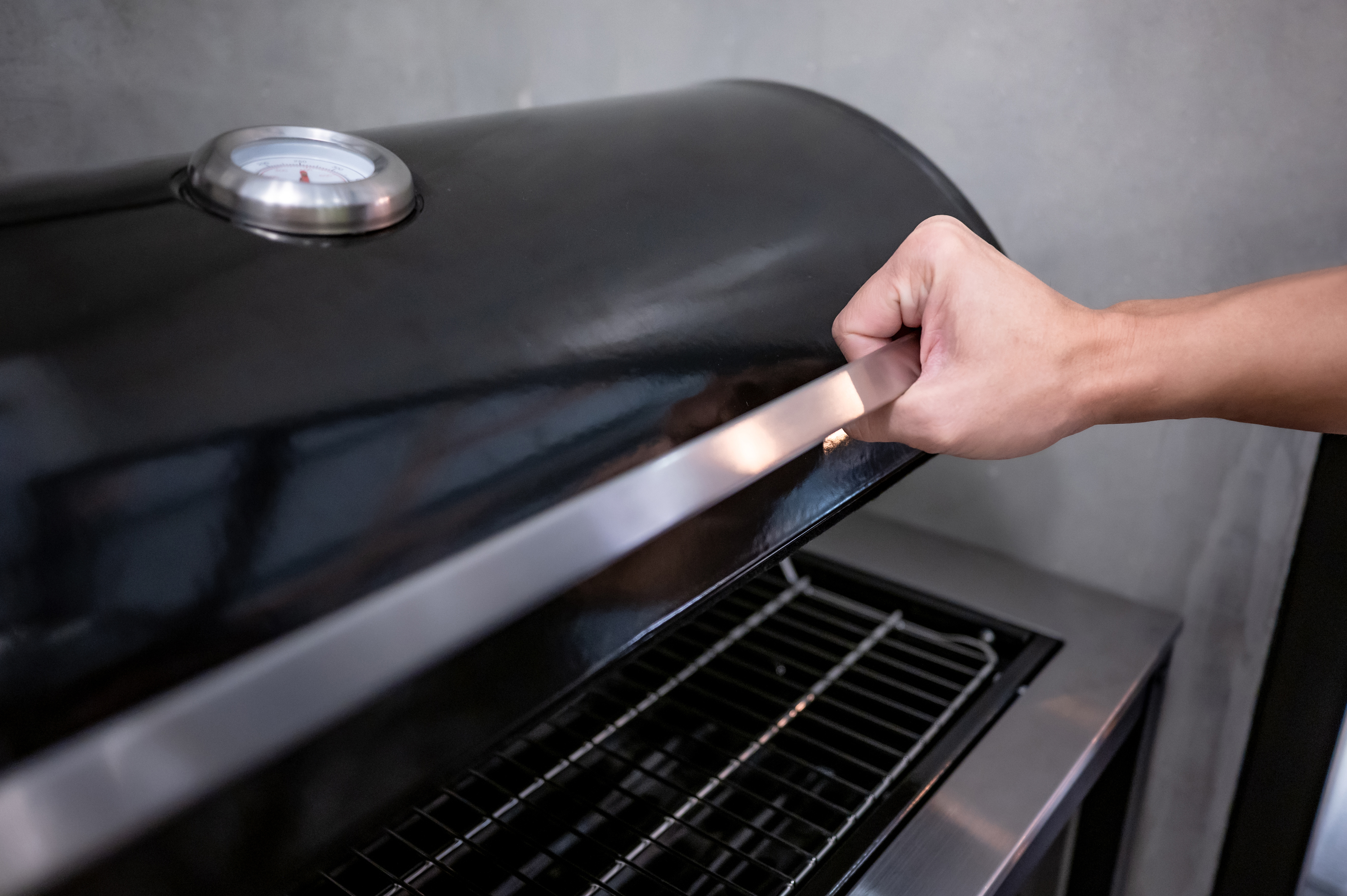 A person lifting the hood of a grill 