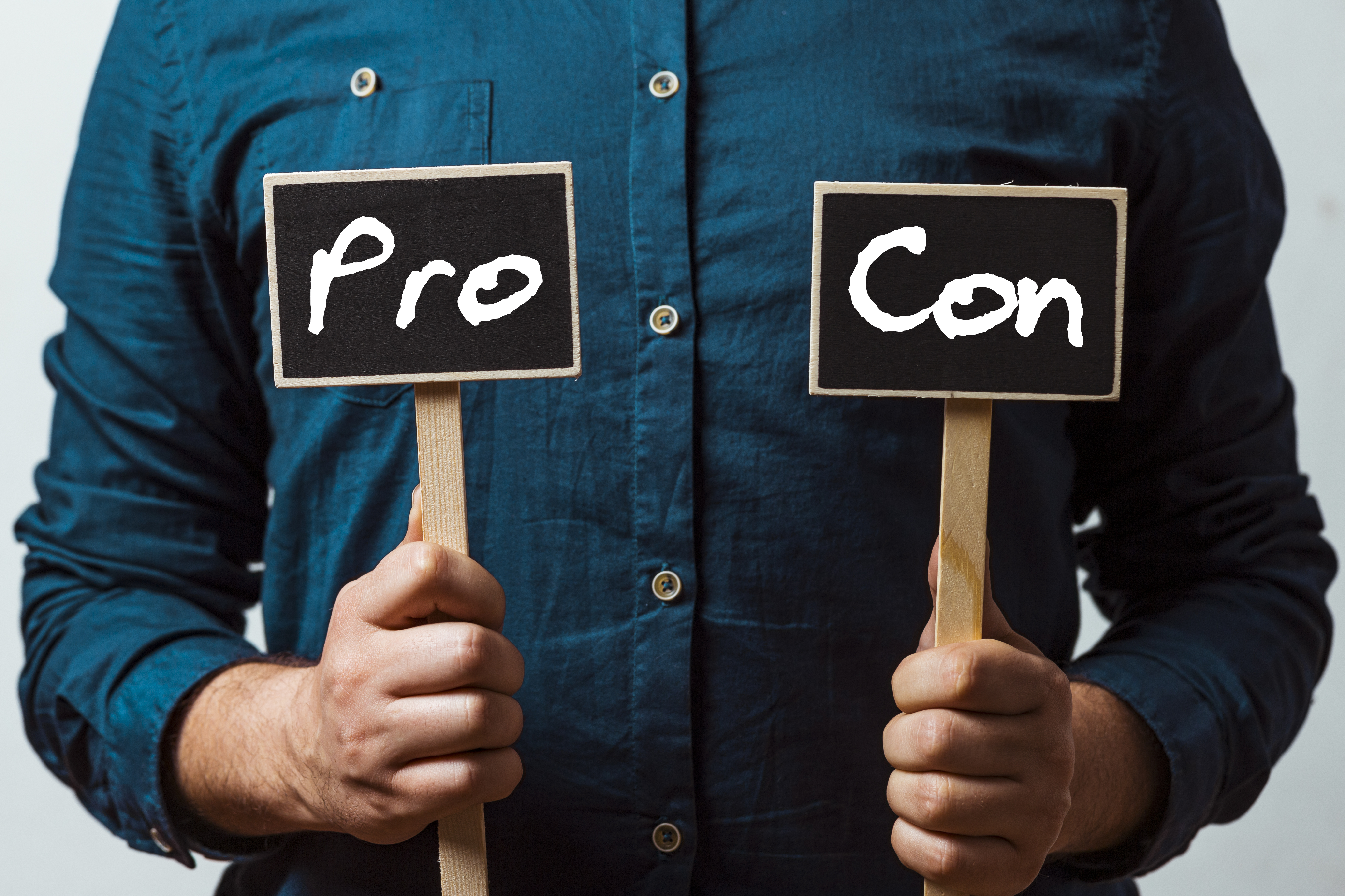 Man in blue button up shirt holding a Pro and Con sign