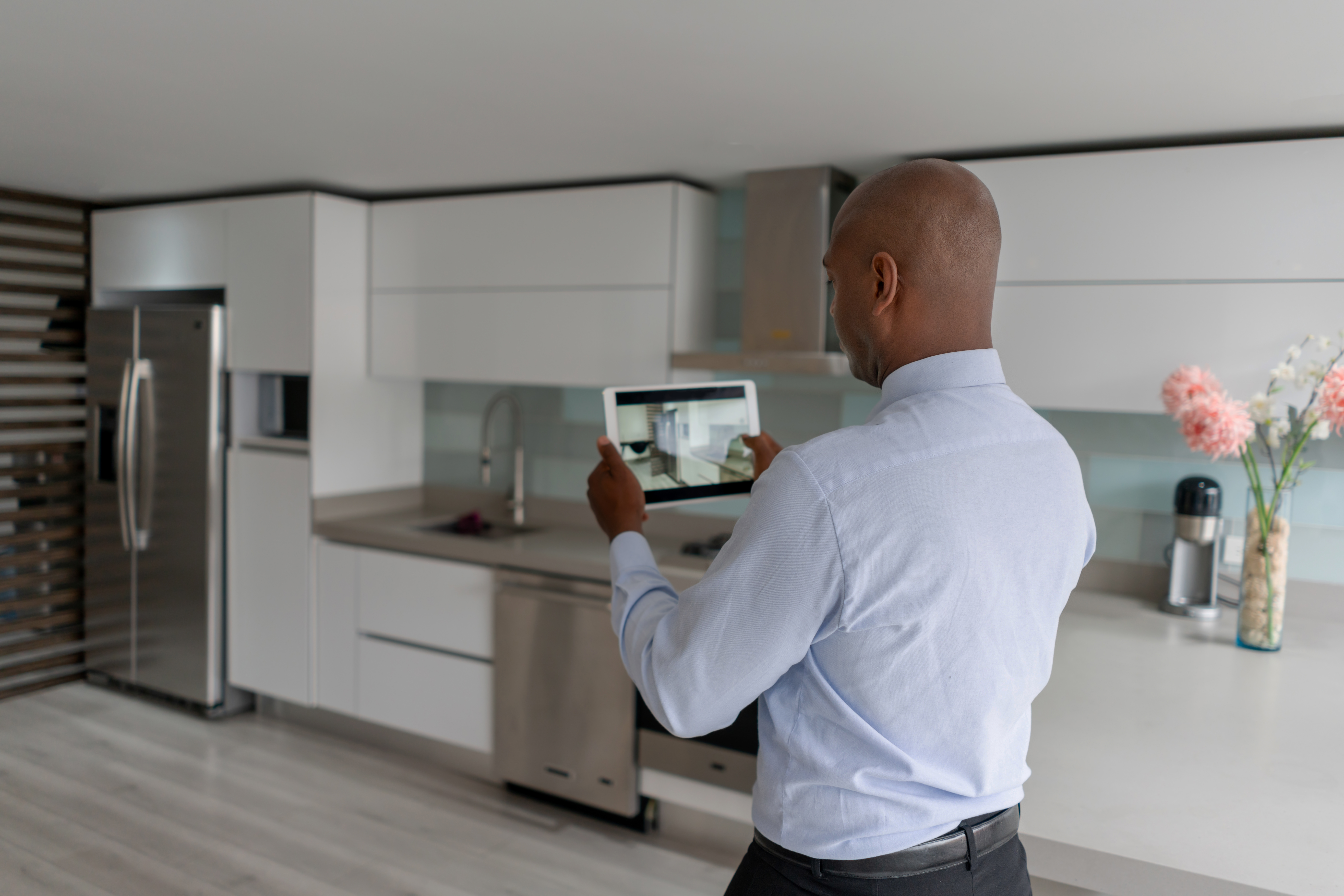 A man dressed in business attire taking a picture of a rental kitchen with a tablet 