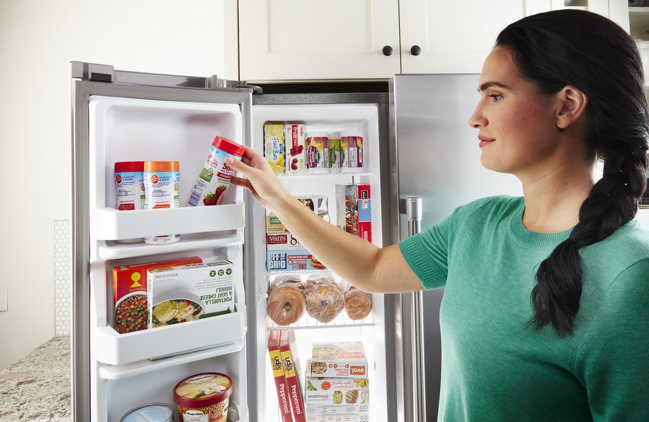 A woman searching for items inside a side by side refrigerator freezer 