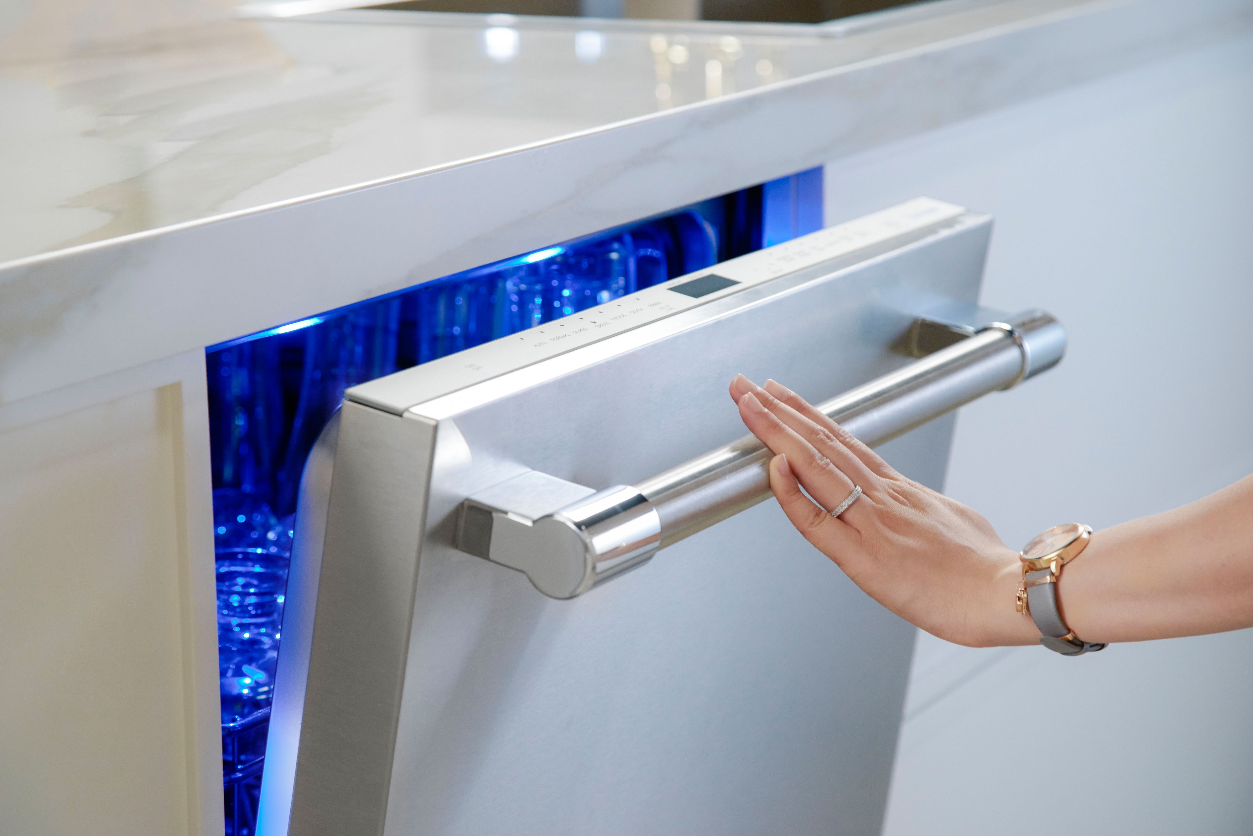 A woman slightly opens a Thermador Sapphire dishwasher with Sapphire Glow interior lighting 