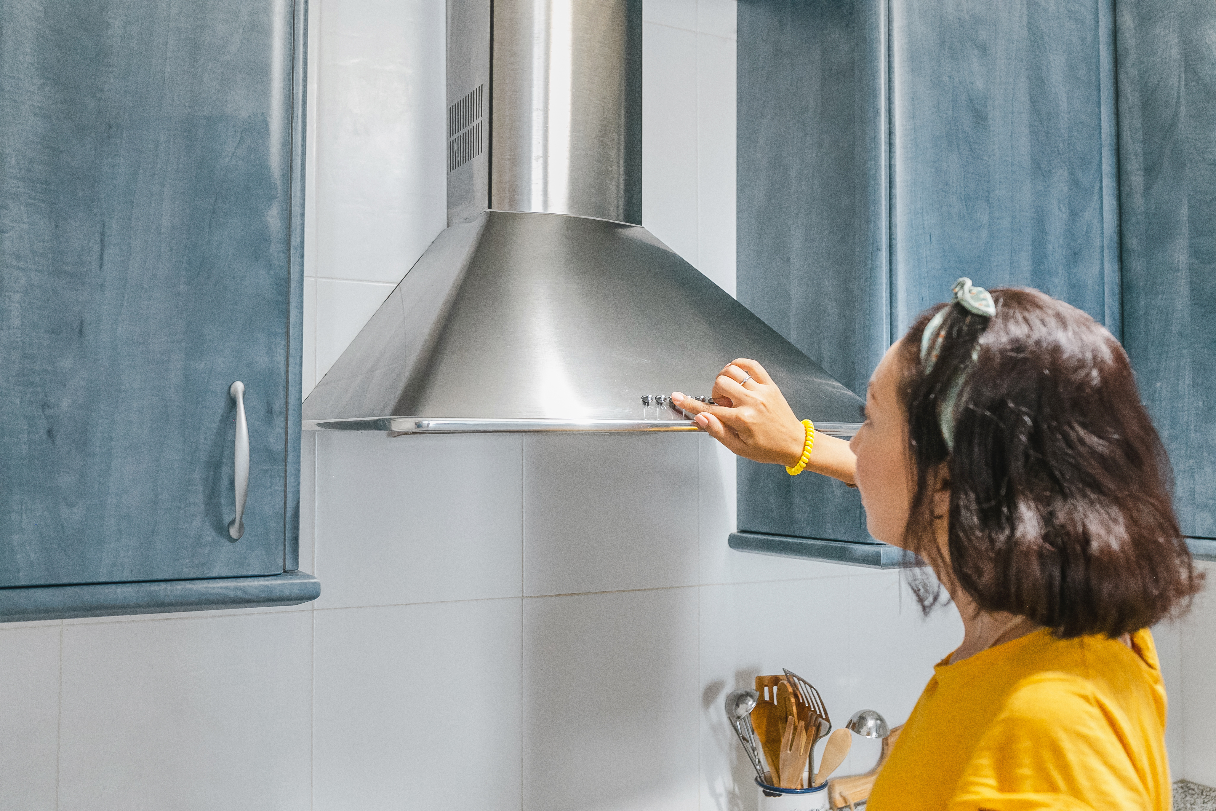 Woman in yellow shirt pressing a button on chimney style over the range hood 
