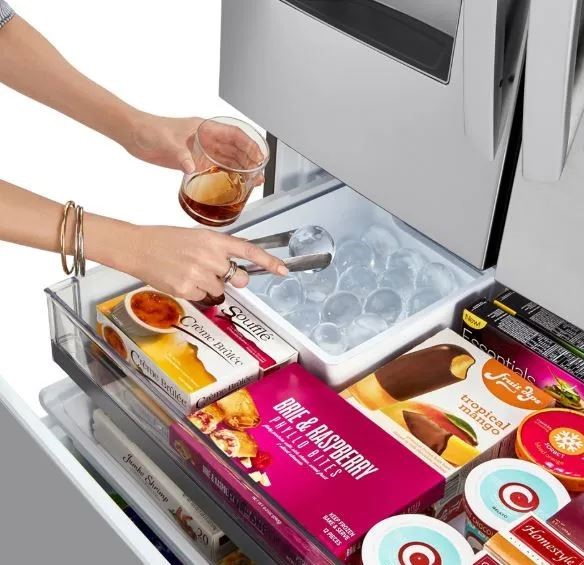 woman hands holding a cup of a dark drink and reaching into ice machine of round ice balls