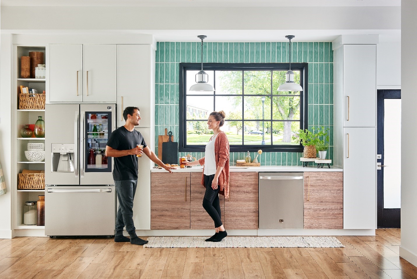 Young man and a woman stand and smile around stainless steel LG kitchen appliances 