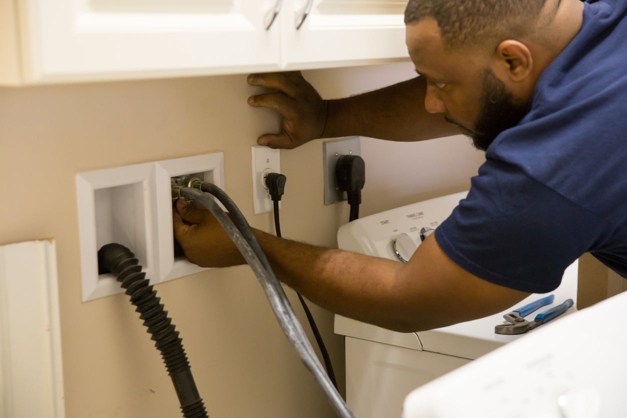 Man in blue shirt connects washer hoses to water feed