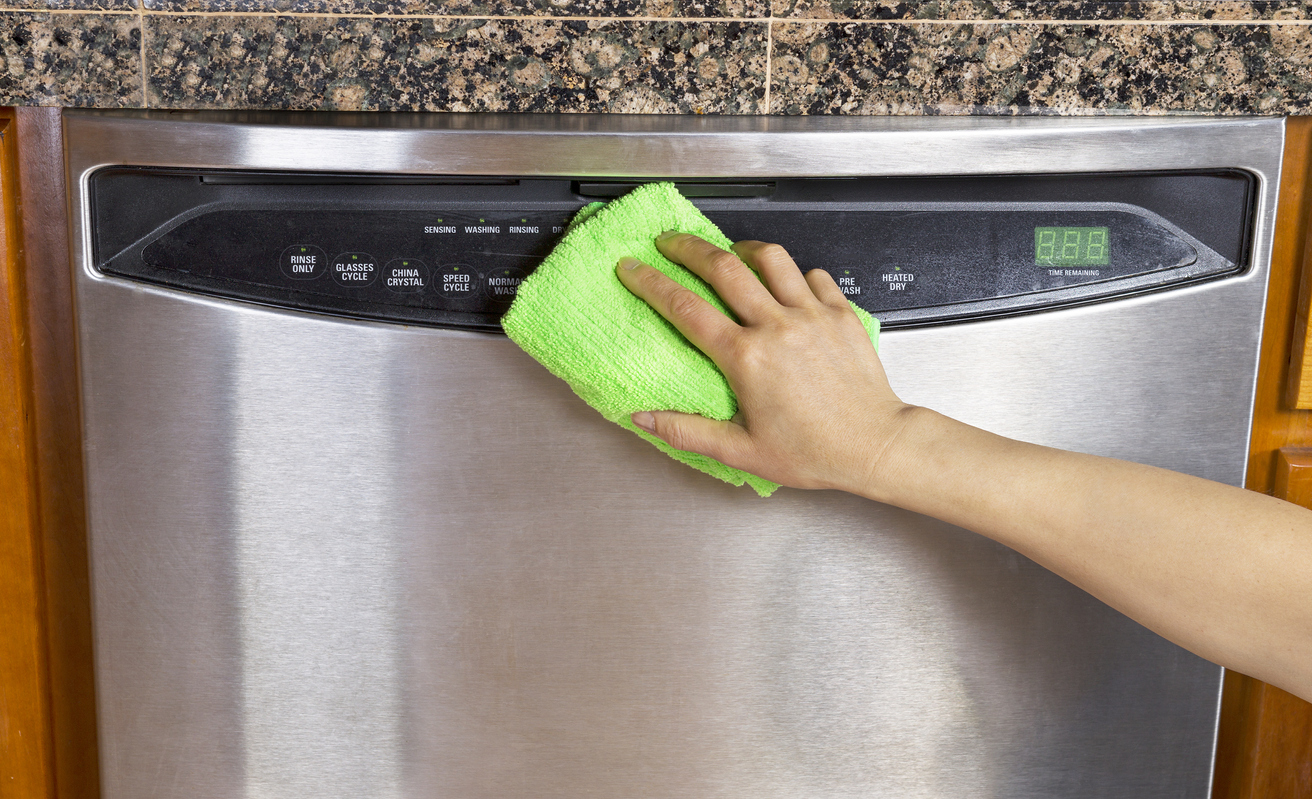 person cleaning a stainless steel dishwasher with a green microfiber cloth