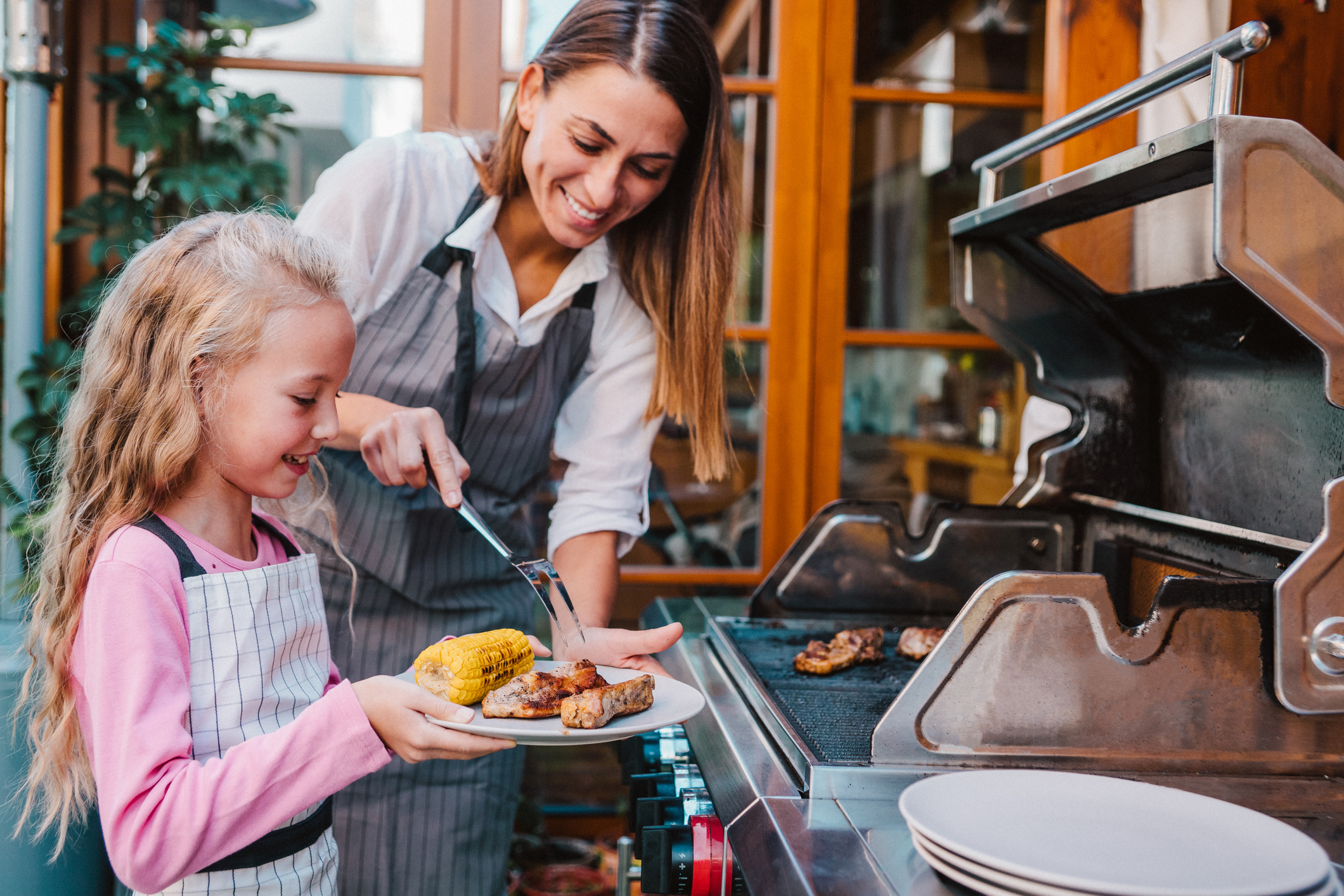 mother taking food off the grill for her daughter